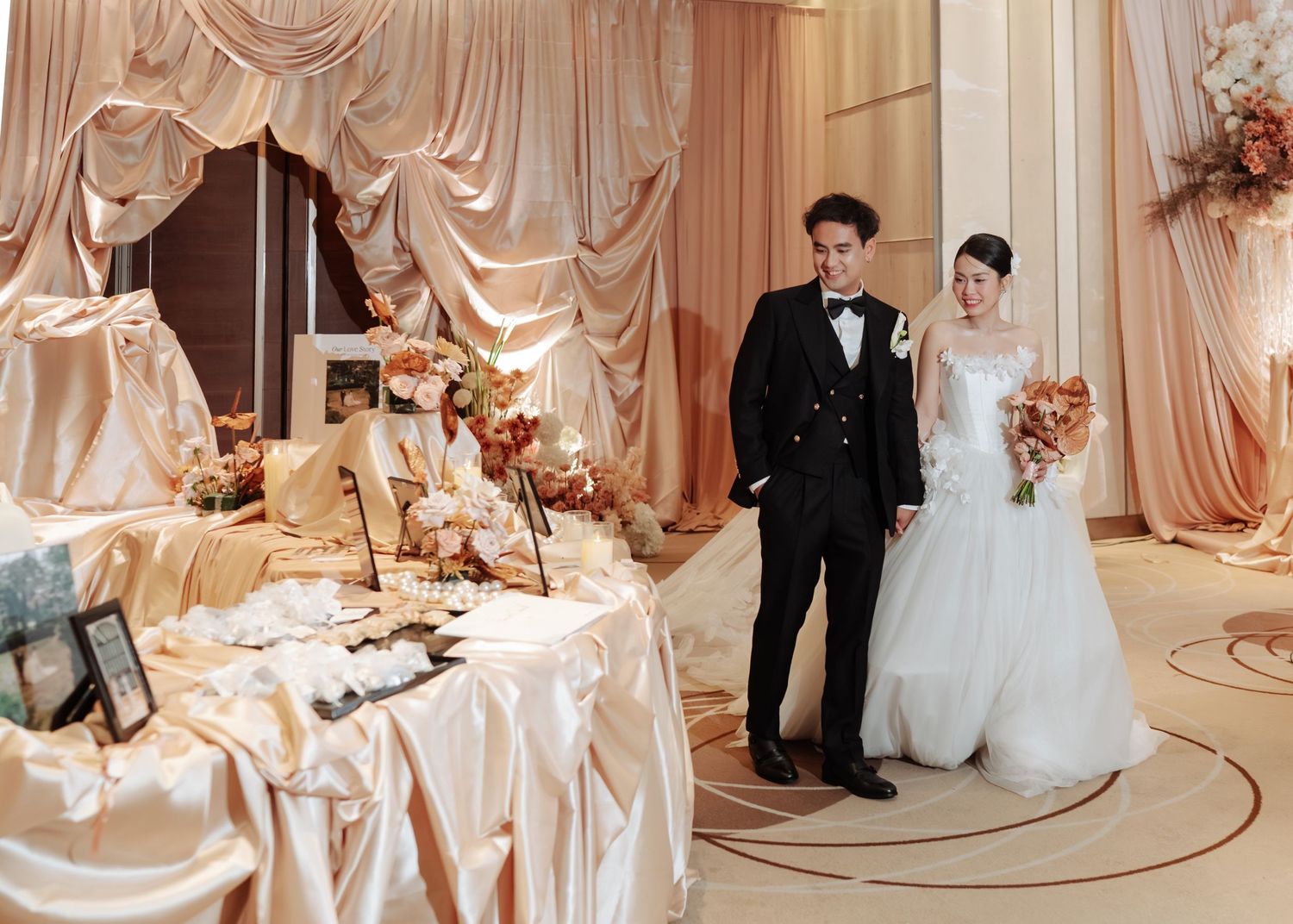 Asian couple at elegant wedding reception venue with gold draping and floral decorations.