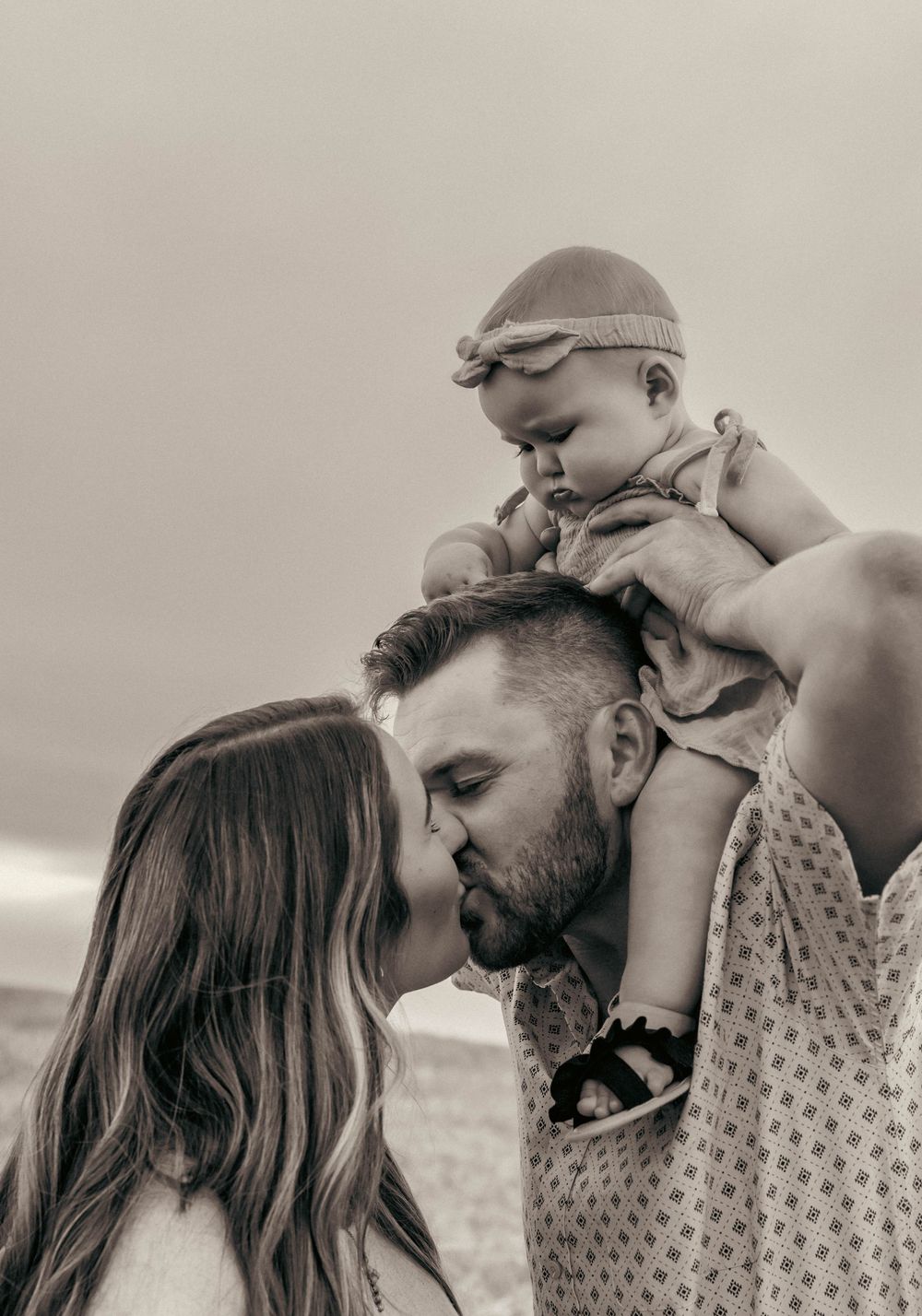 An intimate black and white family portrait showing tender moments with a baby outdoors.