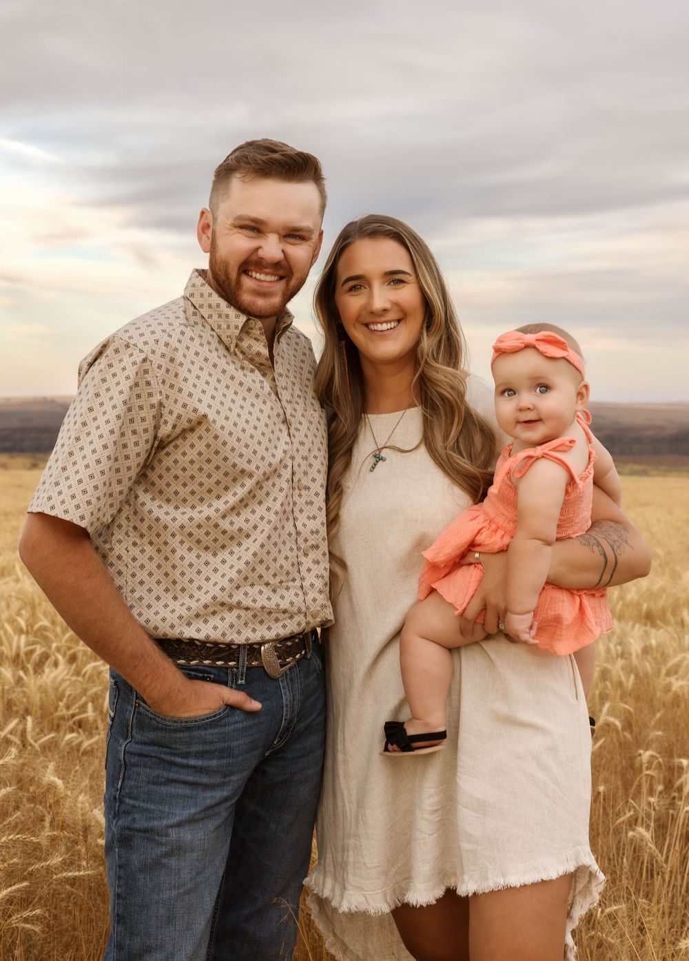 A family poses together in a wheat field during golden hour.