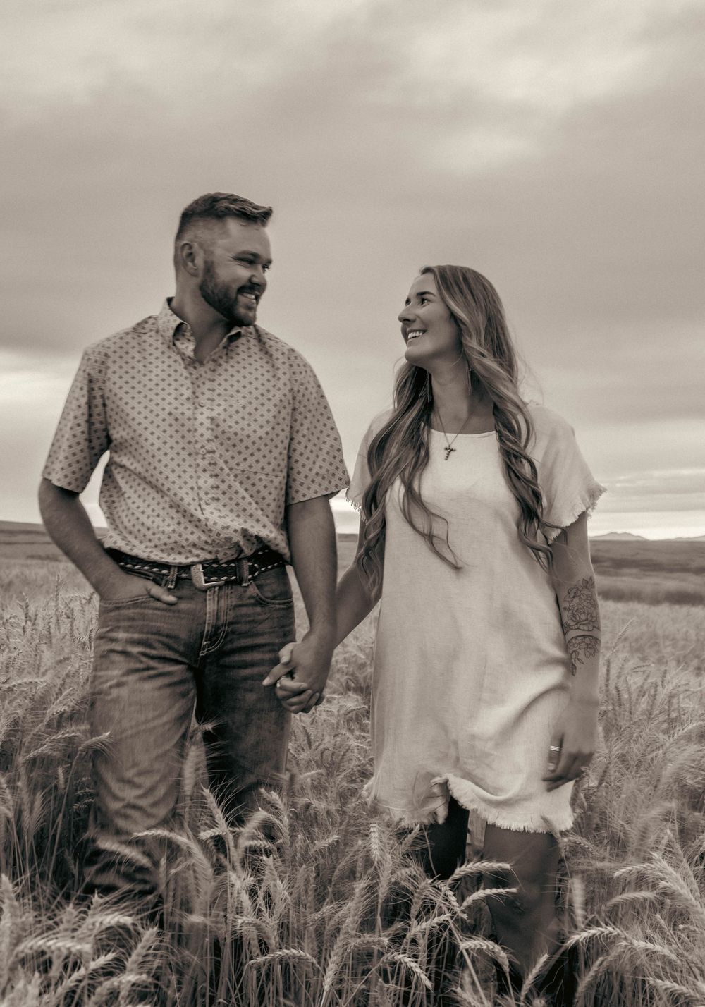 A couple walks hand in hand through a wheat field at sunset.