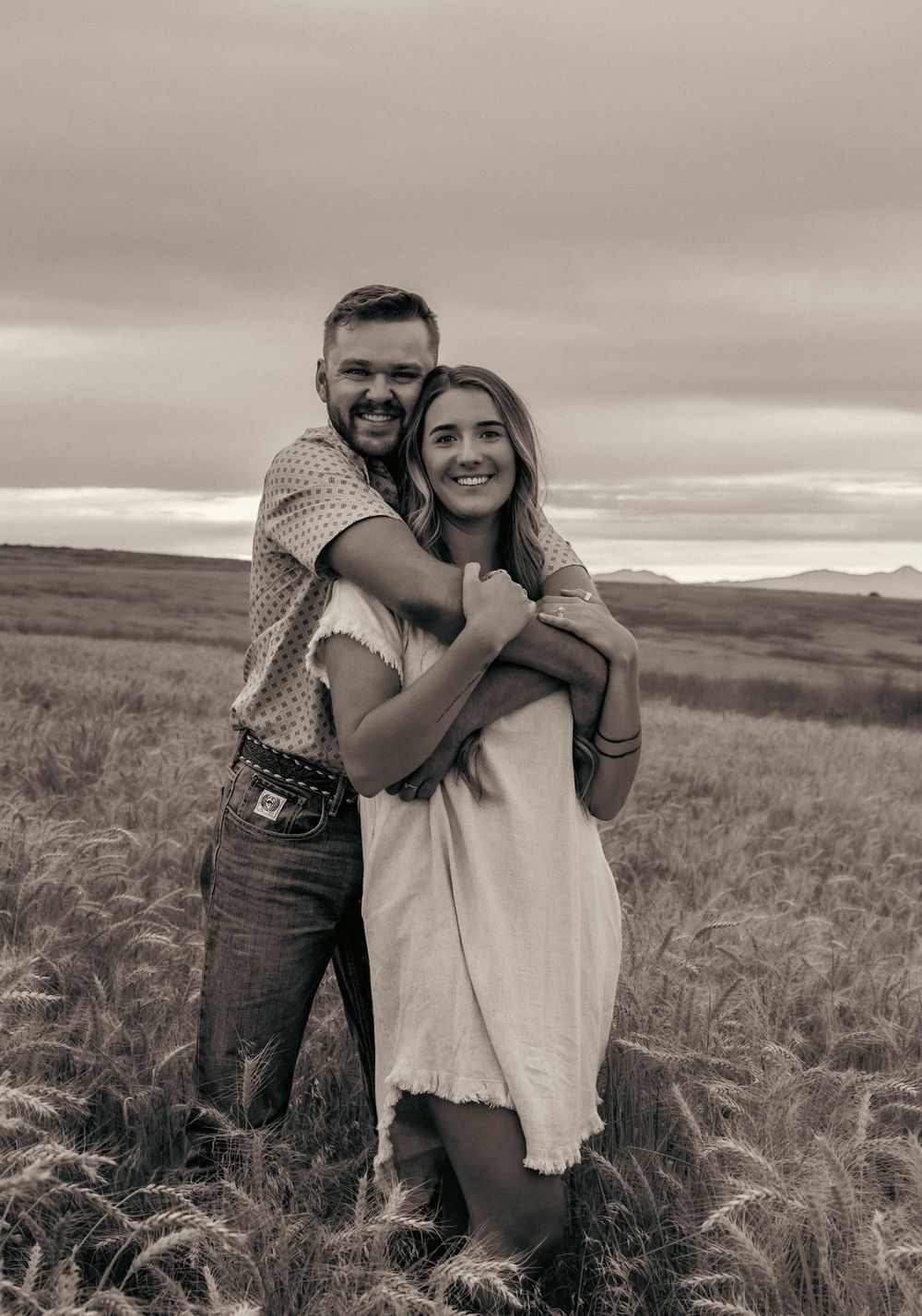A couple embraces joyfully in a golden wheat field during sunset.