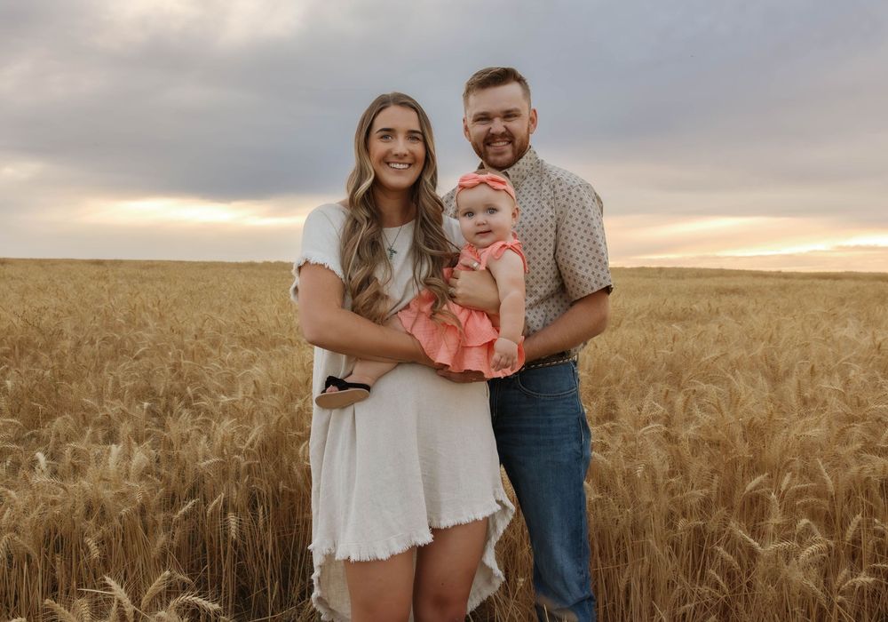 A family shares intimate moments together in a golden wheat field during sunset.