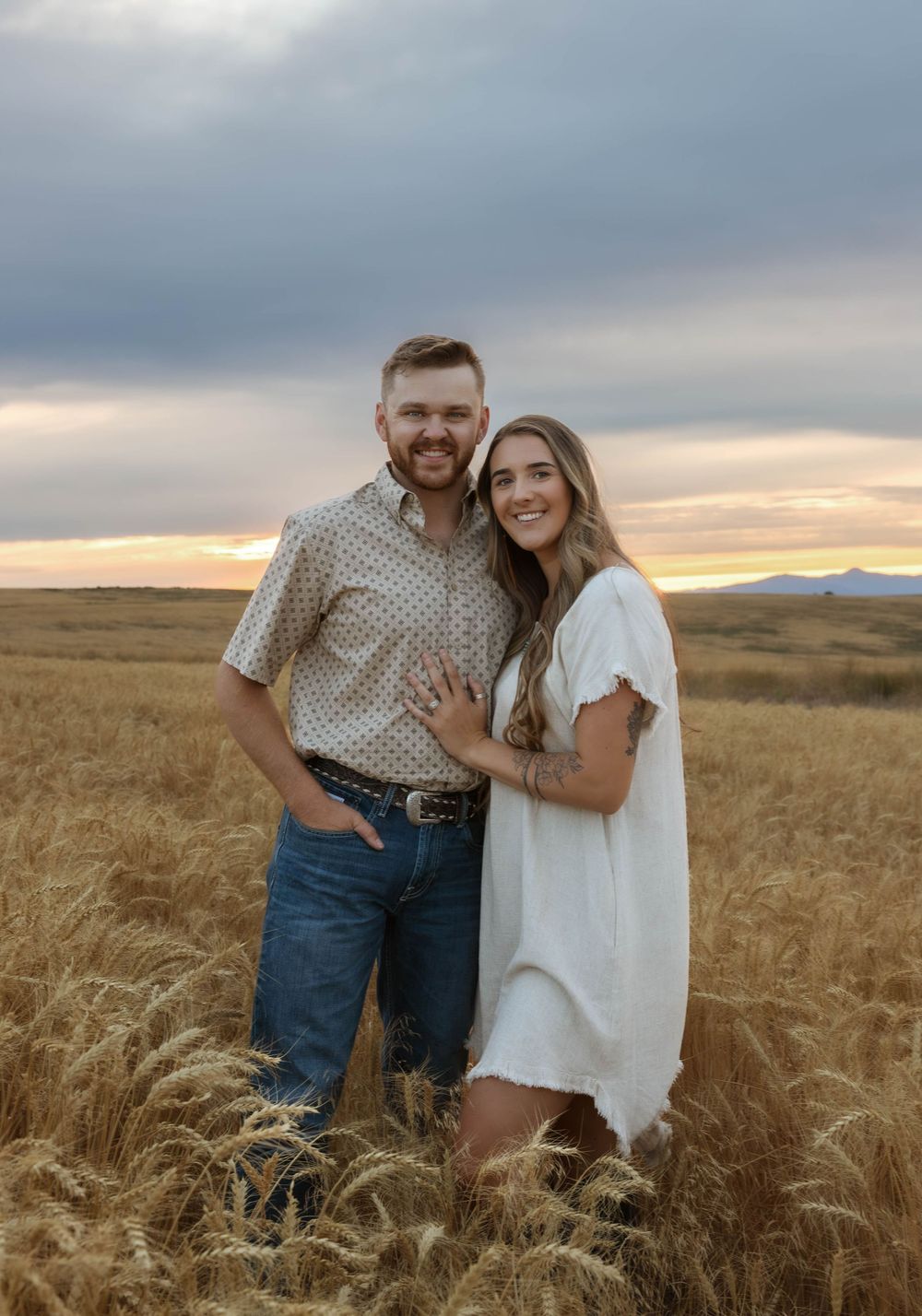 A couple embraces in a golden wheat field during sunset.