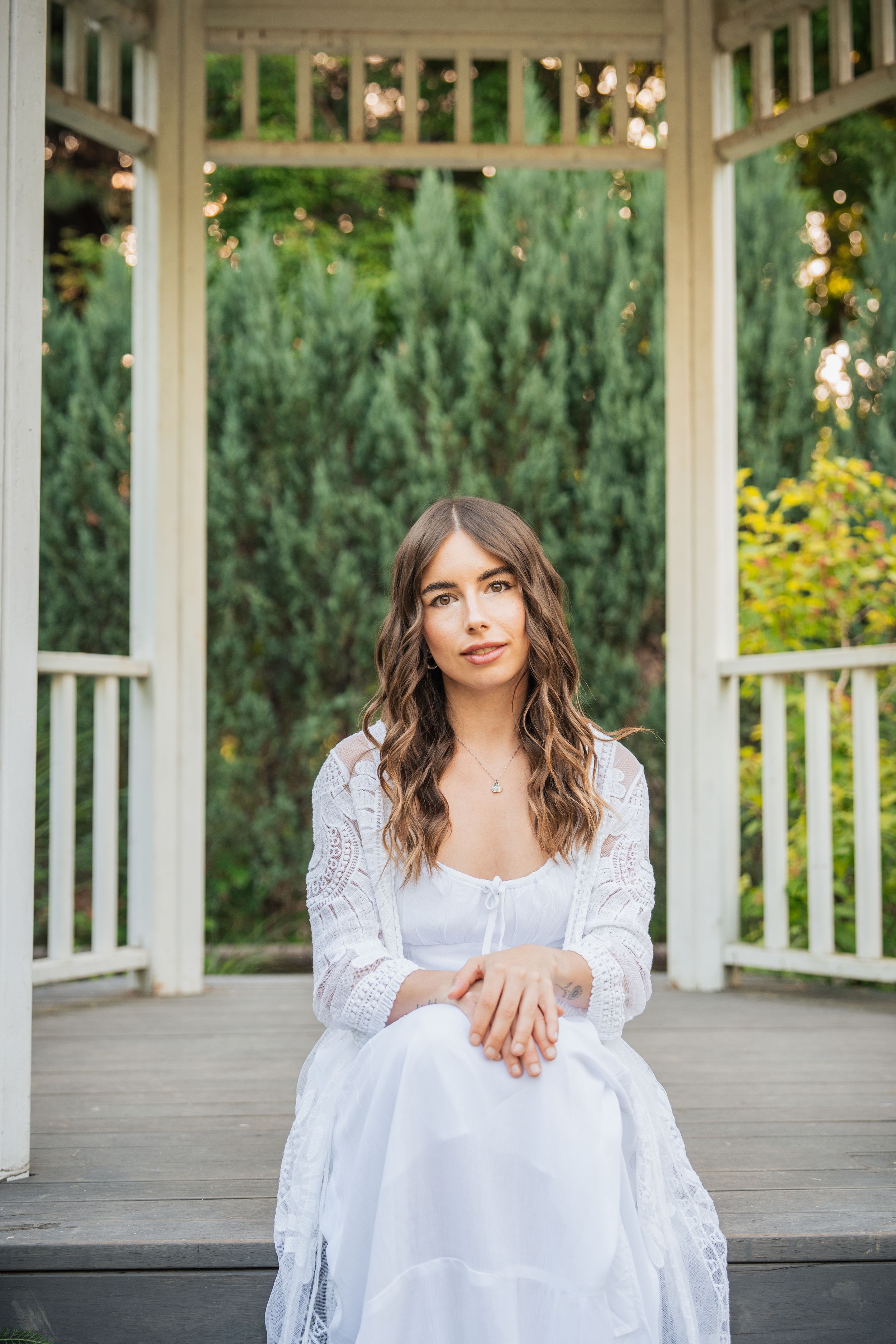 Portrait in white dress at elegant gazebo with garden backdrop.
