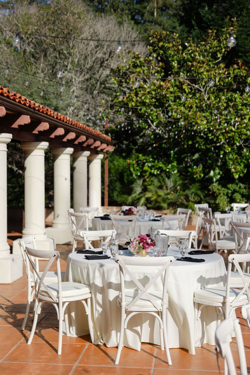 White-clothed tables and chairs arranged on an outdoor terrace patio beneath a covered pergola roof with columns.