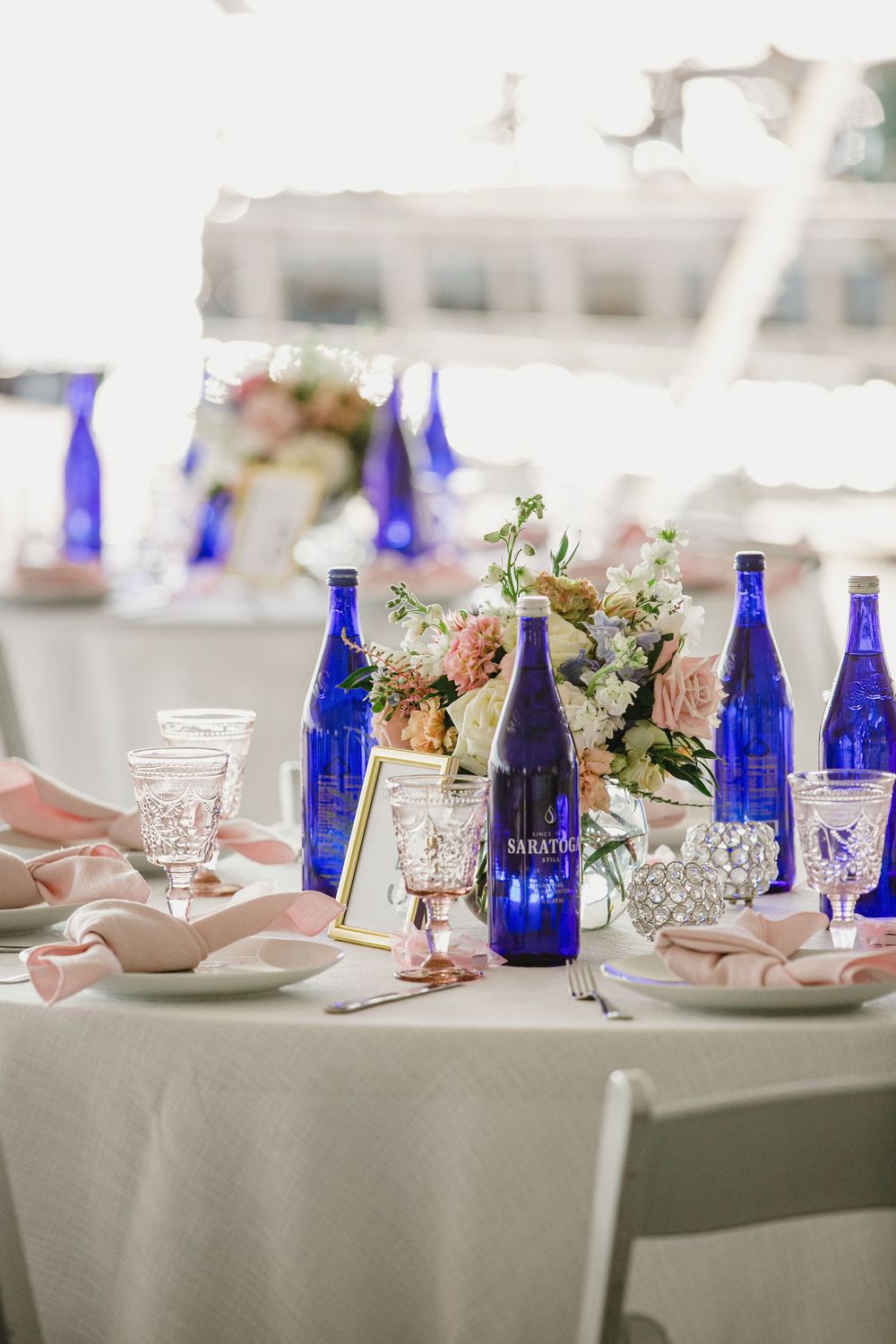 Elegant wedding table setting with cobalt blue glass bottles, pink flowers, and mason jars on white linens. RI Wedding Photographer