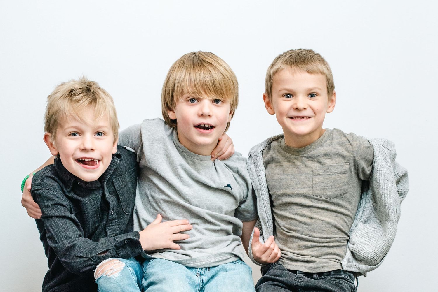 A group of young children sit together smiling while wearing casual clothing in grayscale photos.