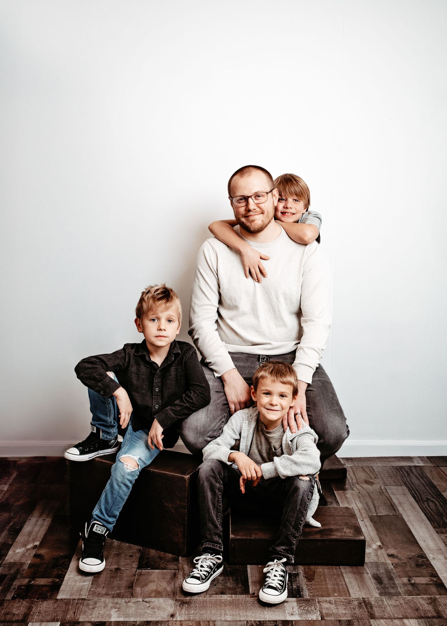 Family portrait of four people sitting together on a wooden bench against a white wall, showcasing casual style.
