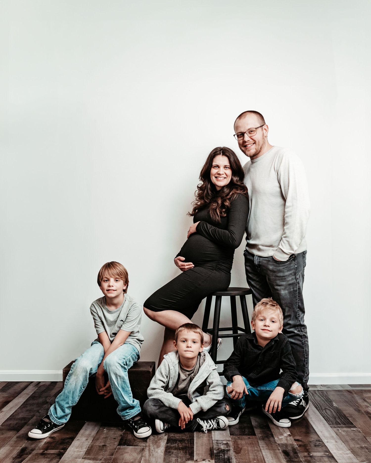 A playful family photo session showing candid moments on a wooden floor against a light gray wall background.
