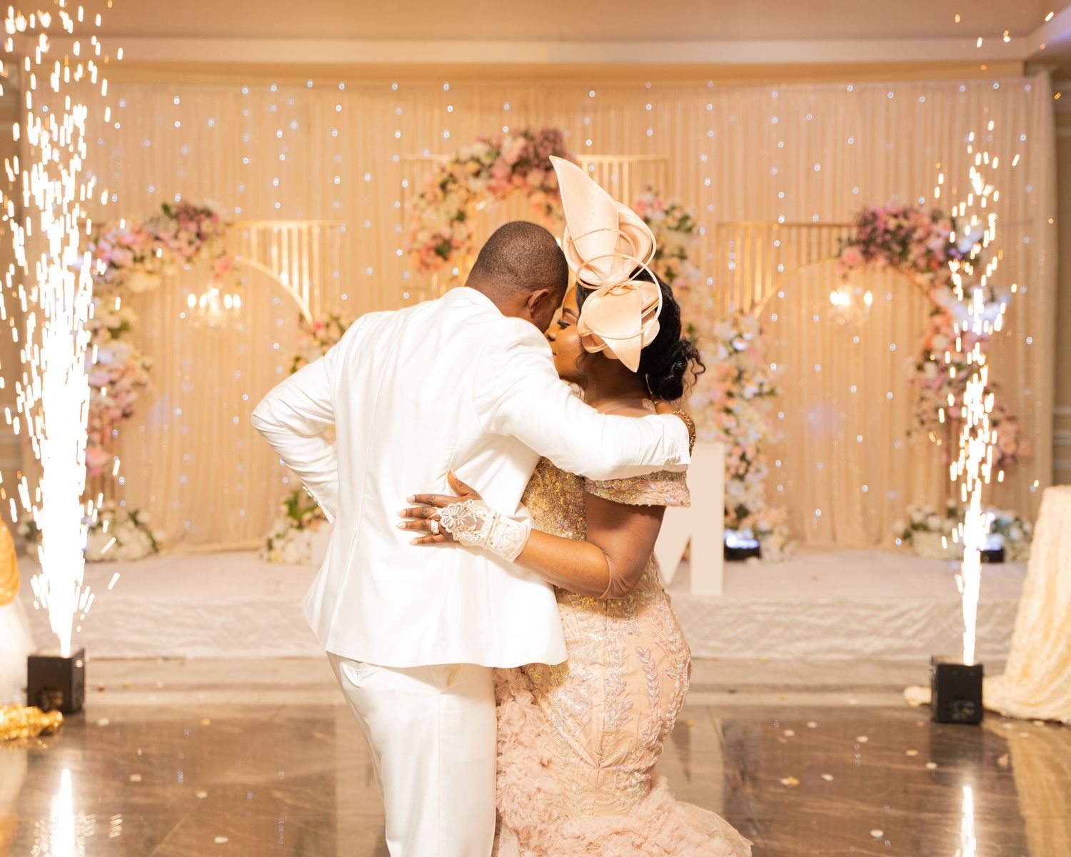 A newlywed couple shares their first dance under sparkling indoor fireworks at an elegant wedding reception.