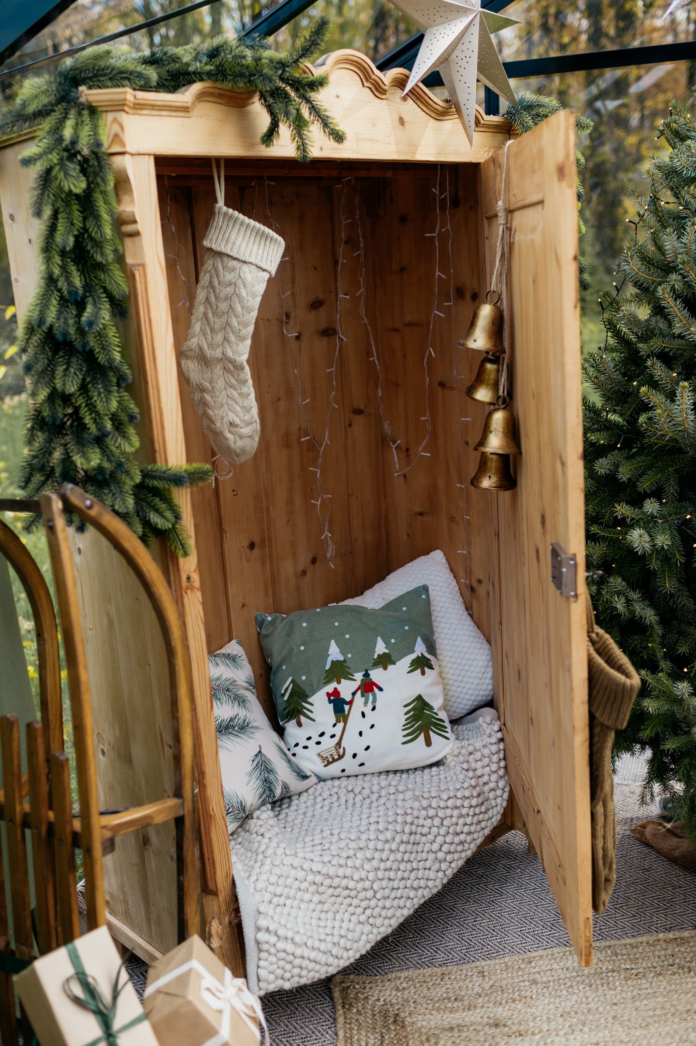 Cozy wooden bench with knitted pillows and Christmas stockings decorated with evergreen branches and holiday decor.