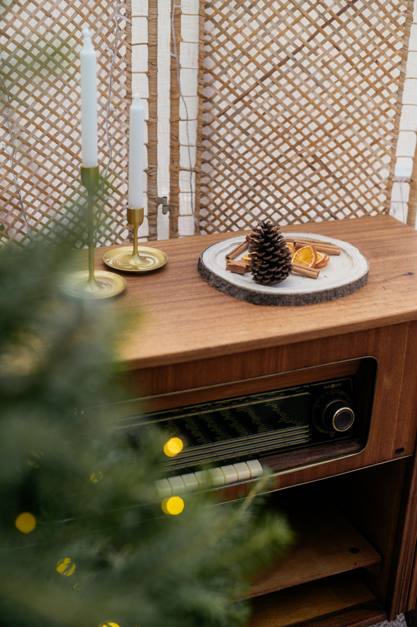 Vintage radio with candles, pinecone and festive decorations on wooden surface against lattice background.