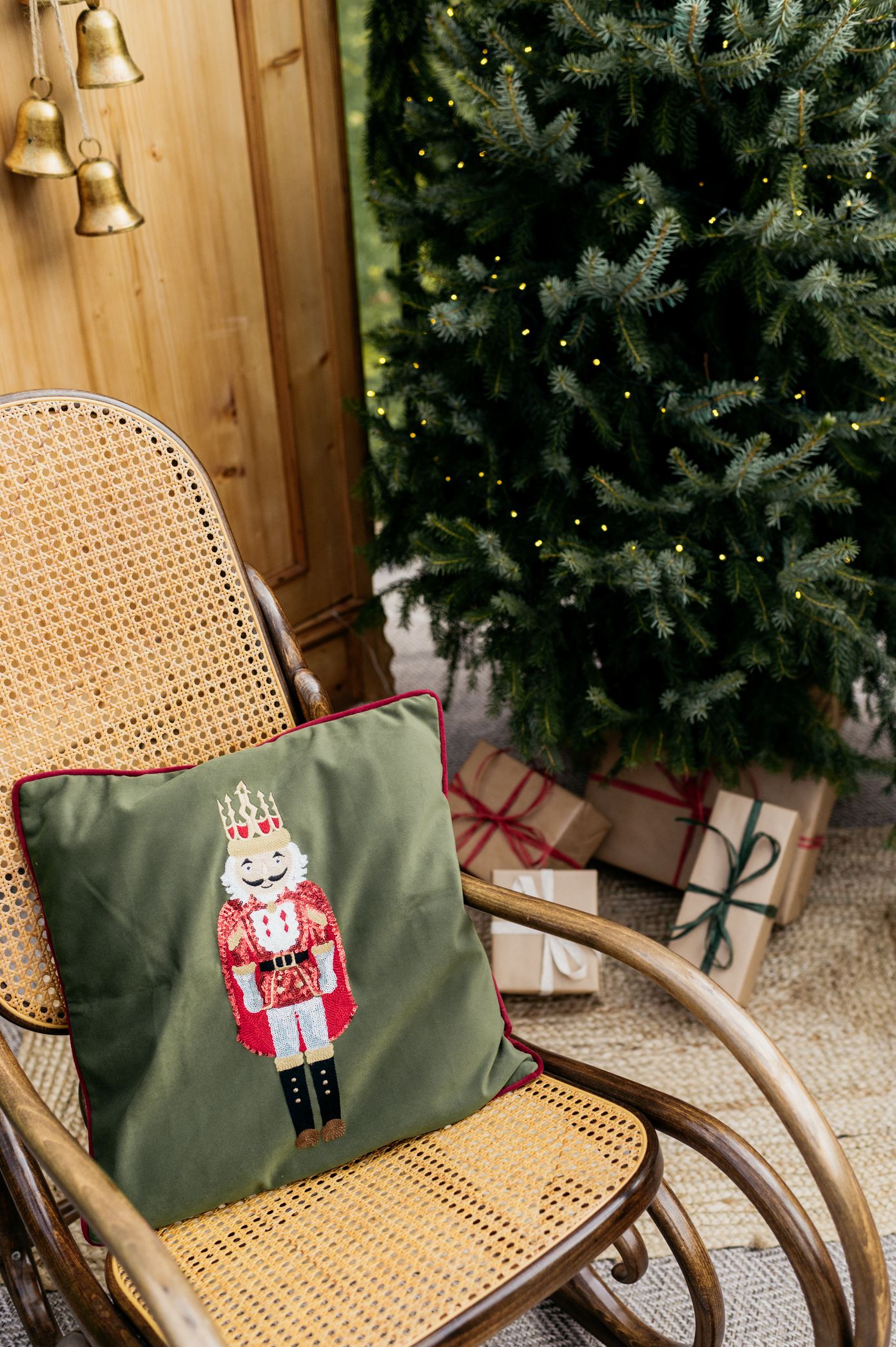 A vintage cane rocking chair with green cushion featuring a nutcracker embroidery sits beside a Christmas tree.