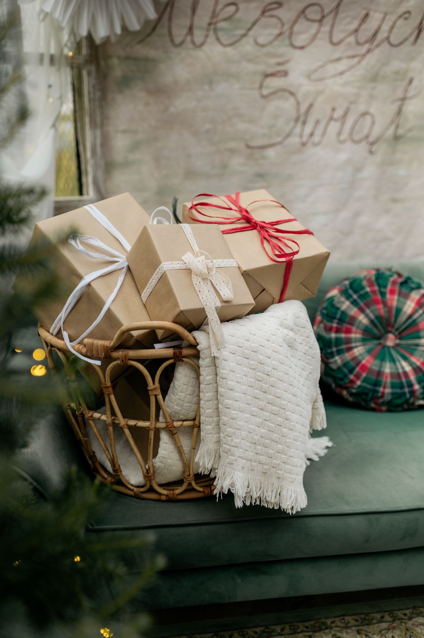 Cozy Christmas scene with kraft paper wrapped gifts, white blanket, and plaid decor arranged on dark surface.