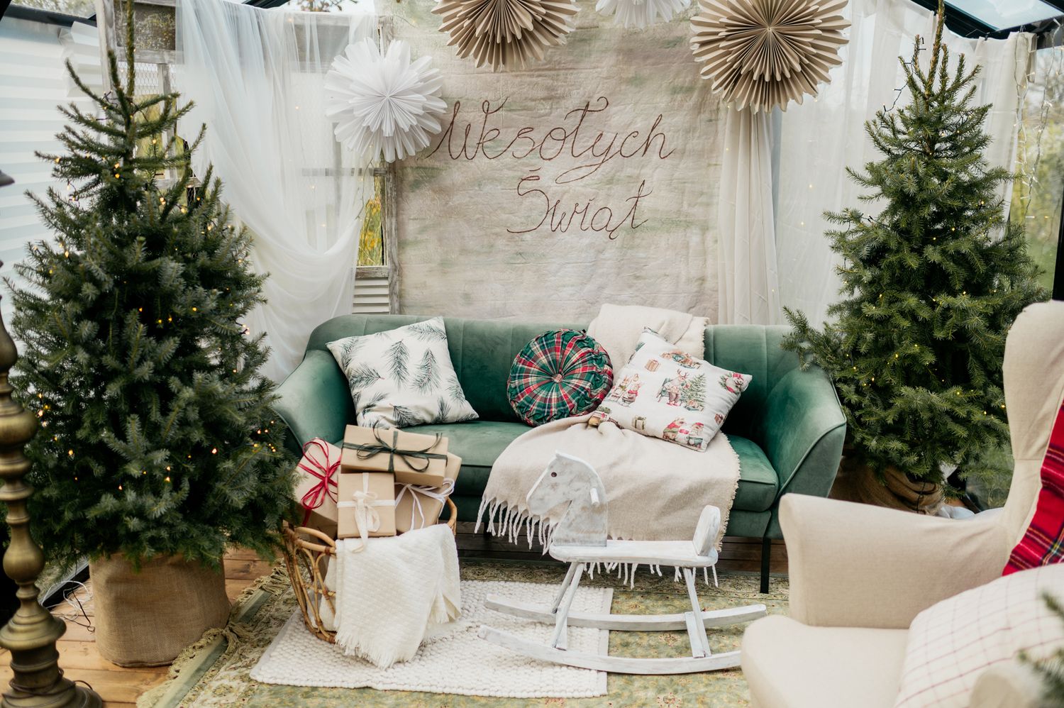 Cozy Christmas decor featuring evergreen trees, white pillows and blankets in a bright interior setting.