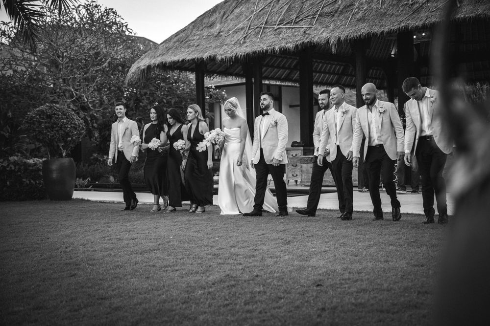 Wedding party members gather outside for formal black and white group photos in an outdoor garden setting.