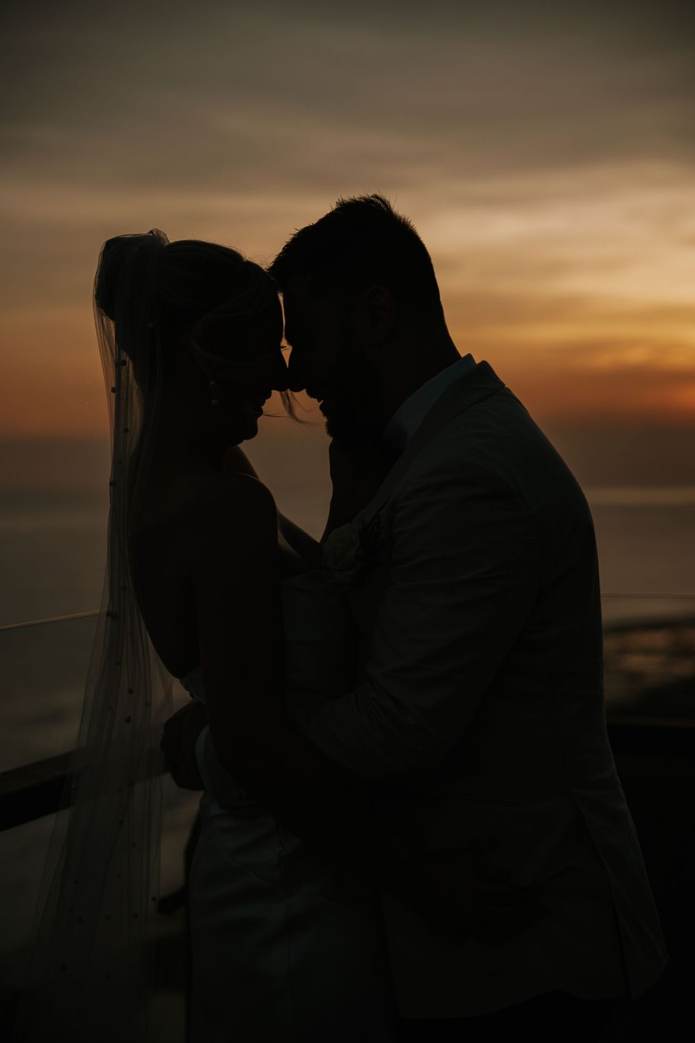 Silhouettes of a romantic couple sharing tender moments at sunset against an ocean backdrop.