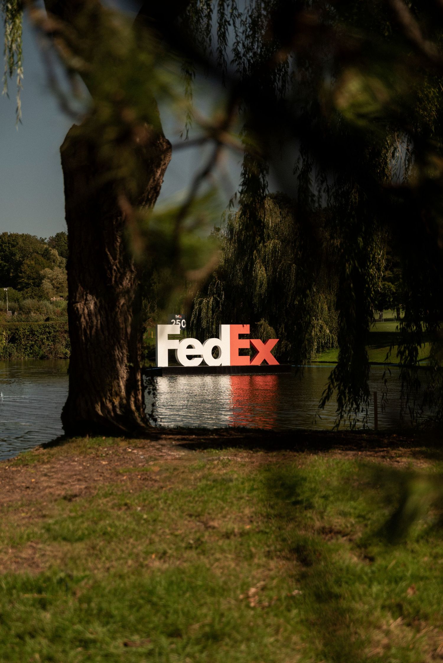 A FedEx logo appears partially visible through trees along a grassy riverbank.