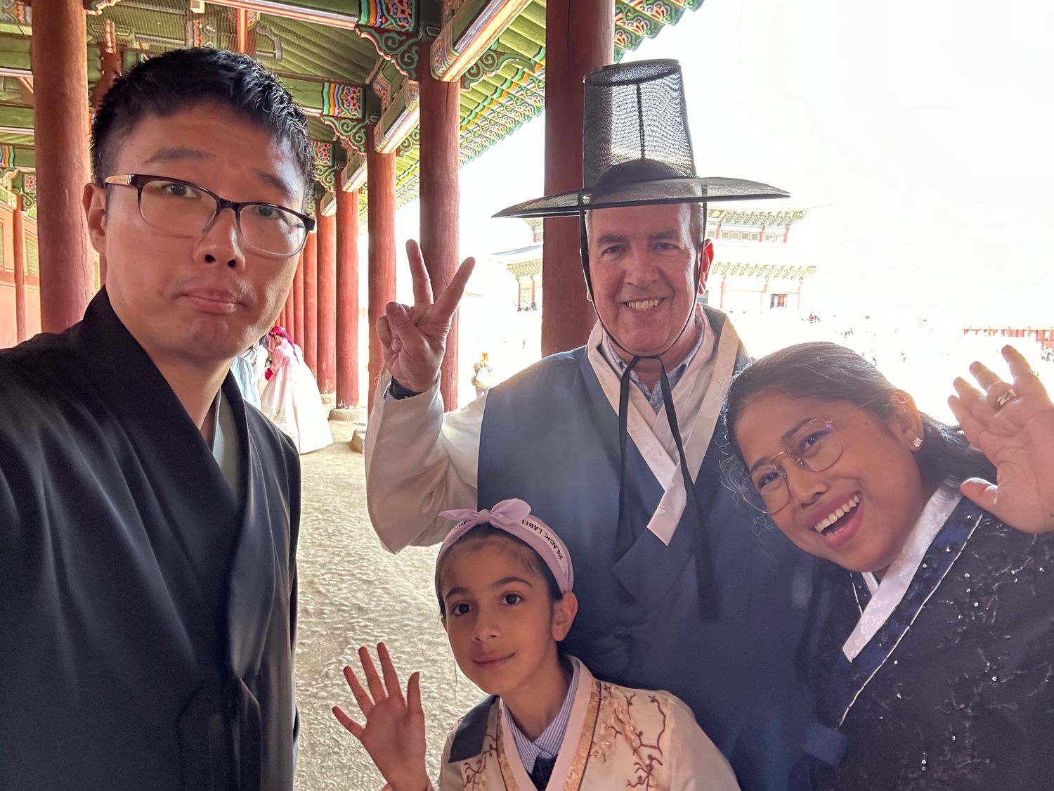 Guests are gathered at a historic Chinese pagoda-style building entrance, posing casually and waving to the camera.