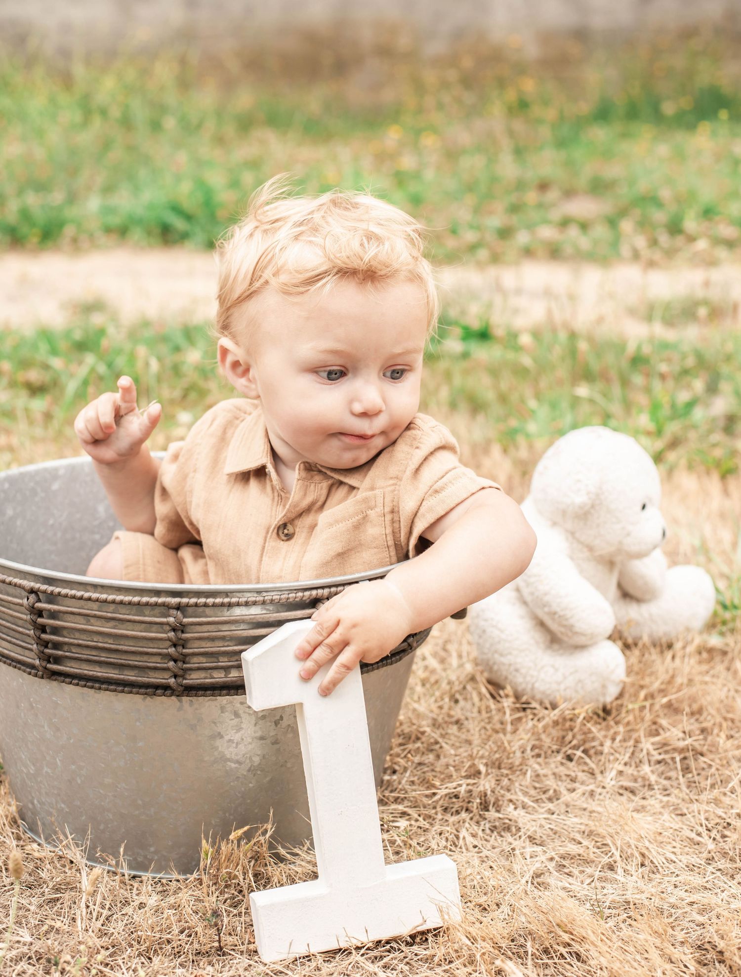 A young child in beige clothing explores a gray concrete planter outdoors in the grass.