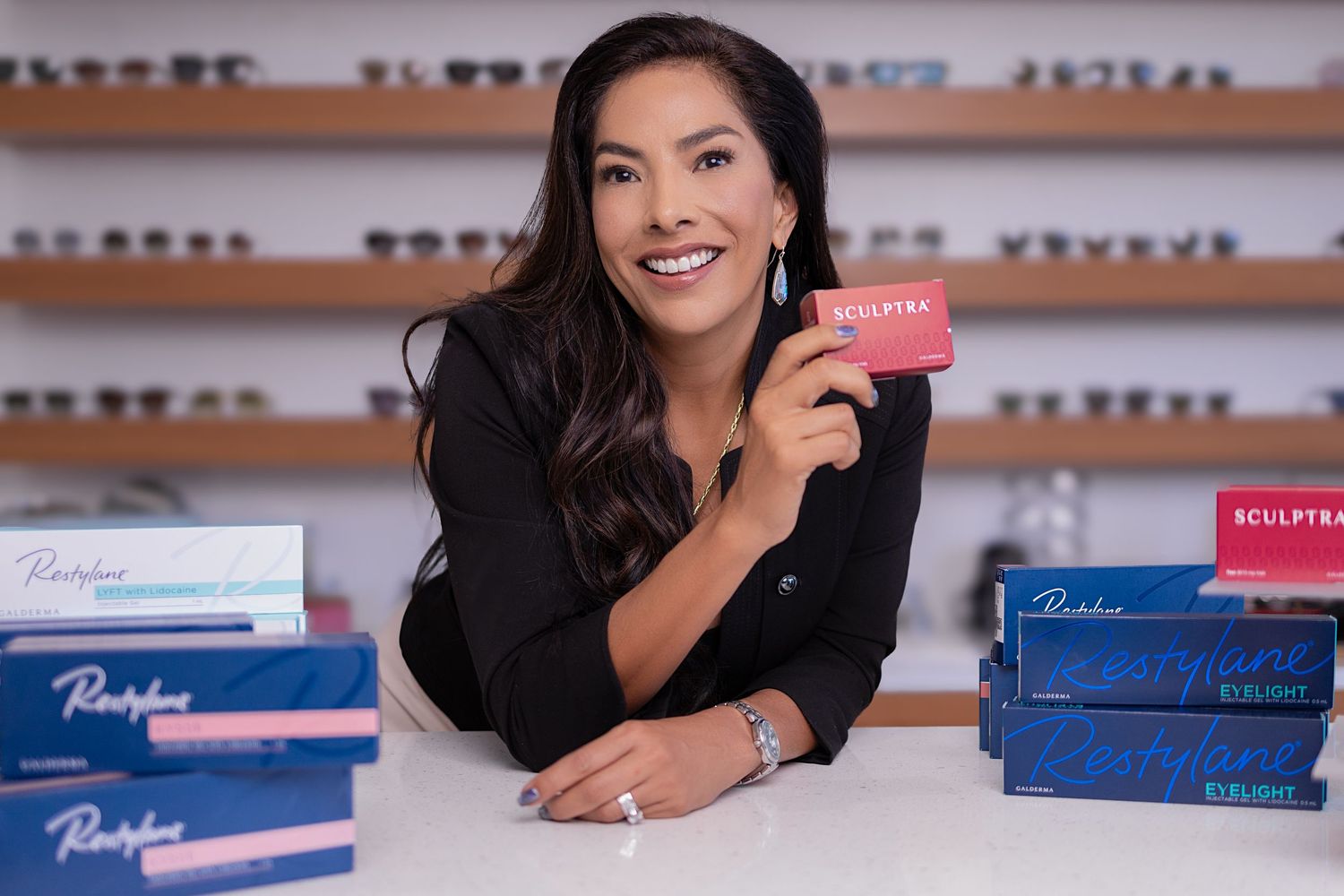 A person smiles while lying on the floor next to stacks of blue contact lens boxes in an optical store display.