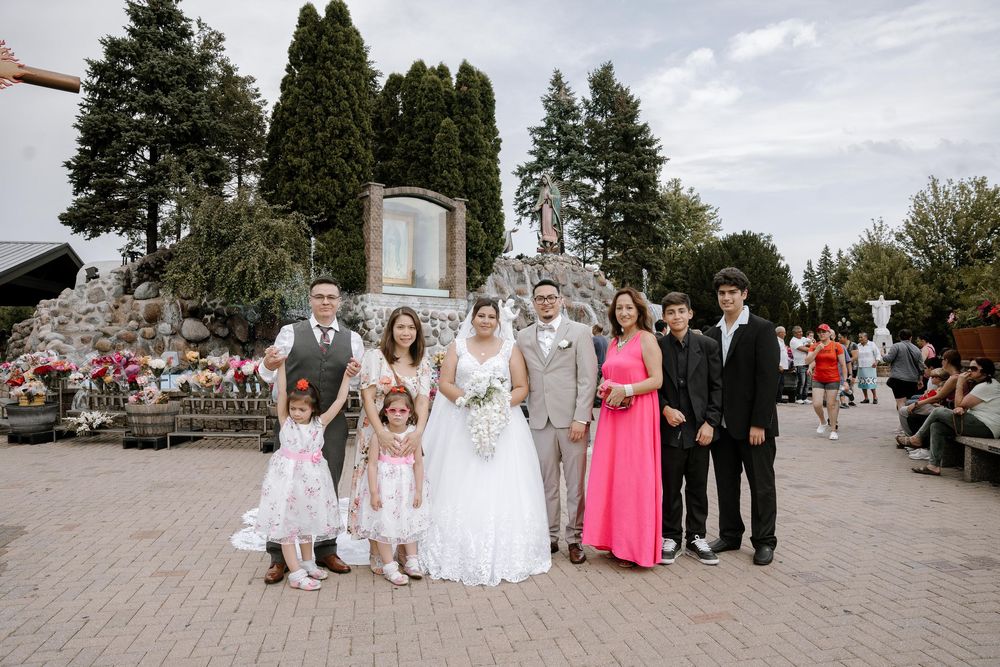 A wedding party poses outdoors on stone steps surrounded by evergreen trees in the background.