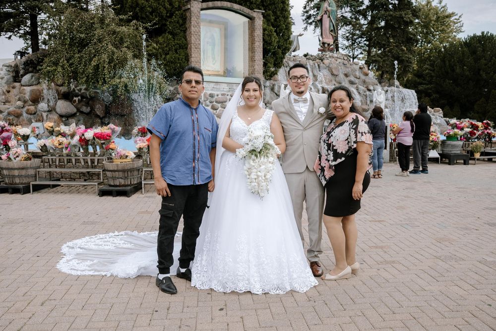 A wedding party poses together in front of a stone wall decorated with red flowers.