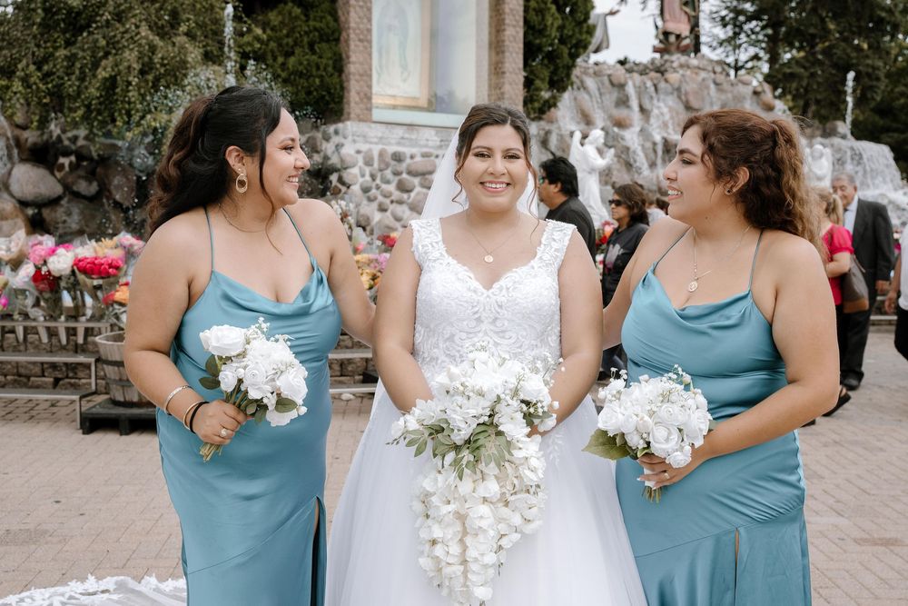 Three women in formal attire share a joyful moment at outdoor wedding celebration.