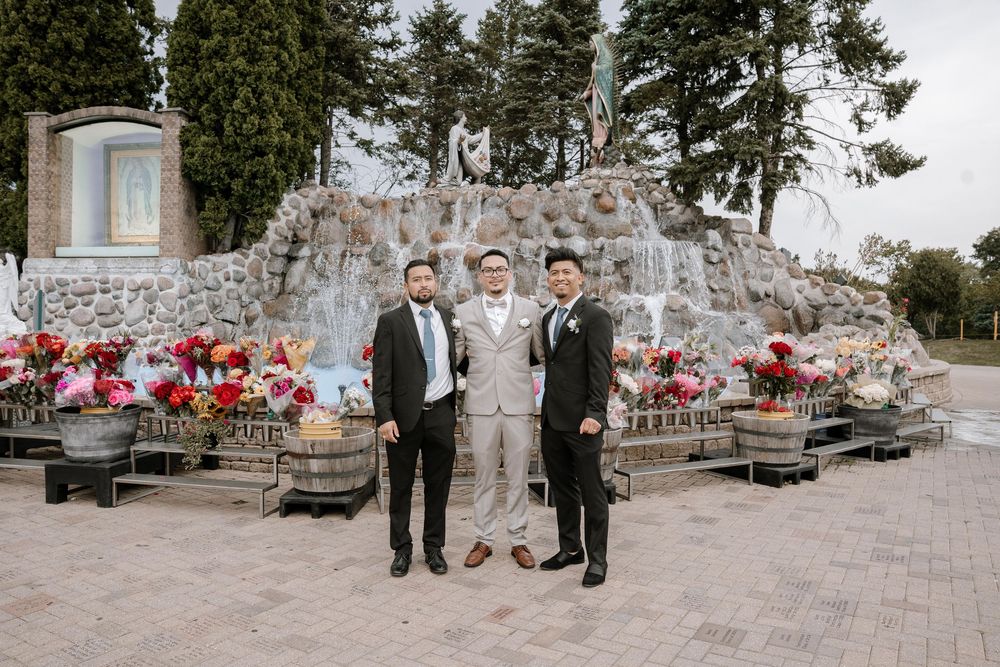 Wedding group stands on stone patio with trees and stone wall backdrop.