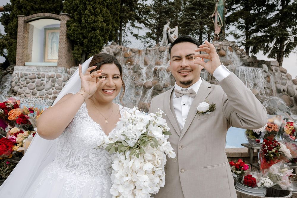 Newlyweds share a playful moment while posing in front of floral decorations outdoors.