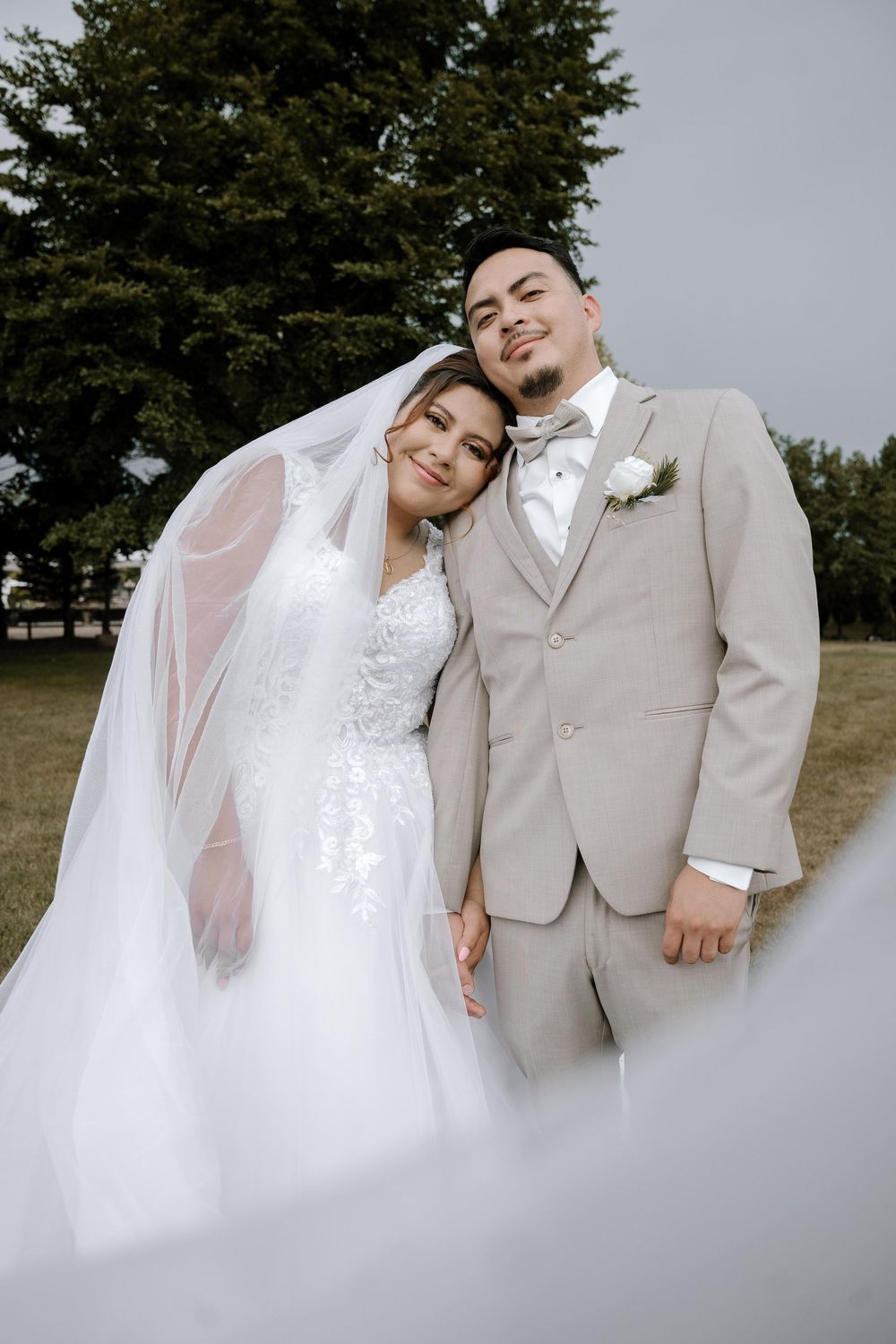Newlyweds pose together outdoors with evergreen trees in background.