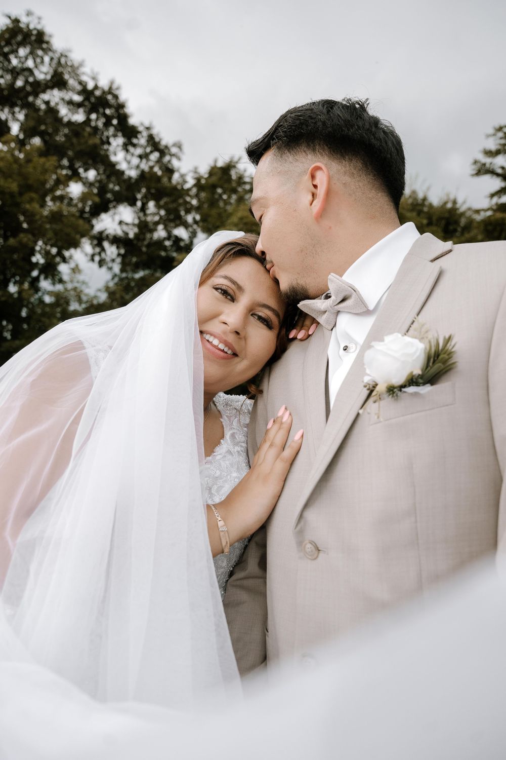 Close-up wedding portrait with flowing white veil in natural outdoor setting.