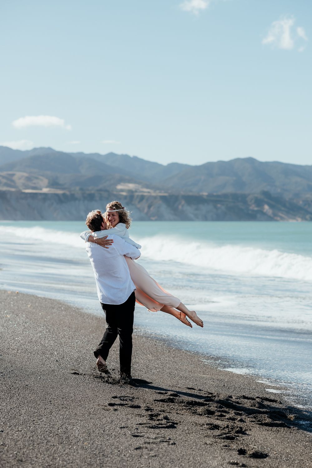 A couple enjoys a playful moment together on Whangaimoana beach Wairarapa with mountains visible in the background by August and Vine