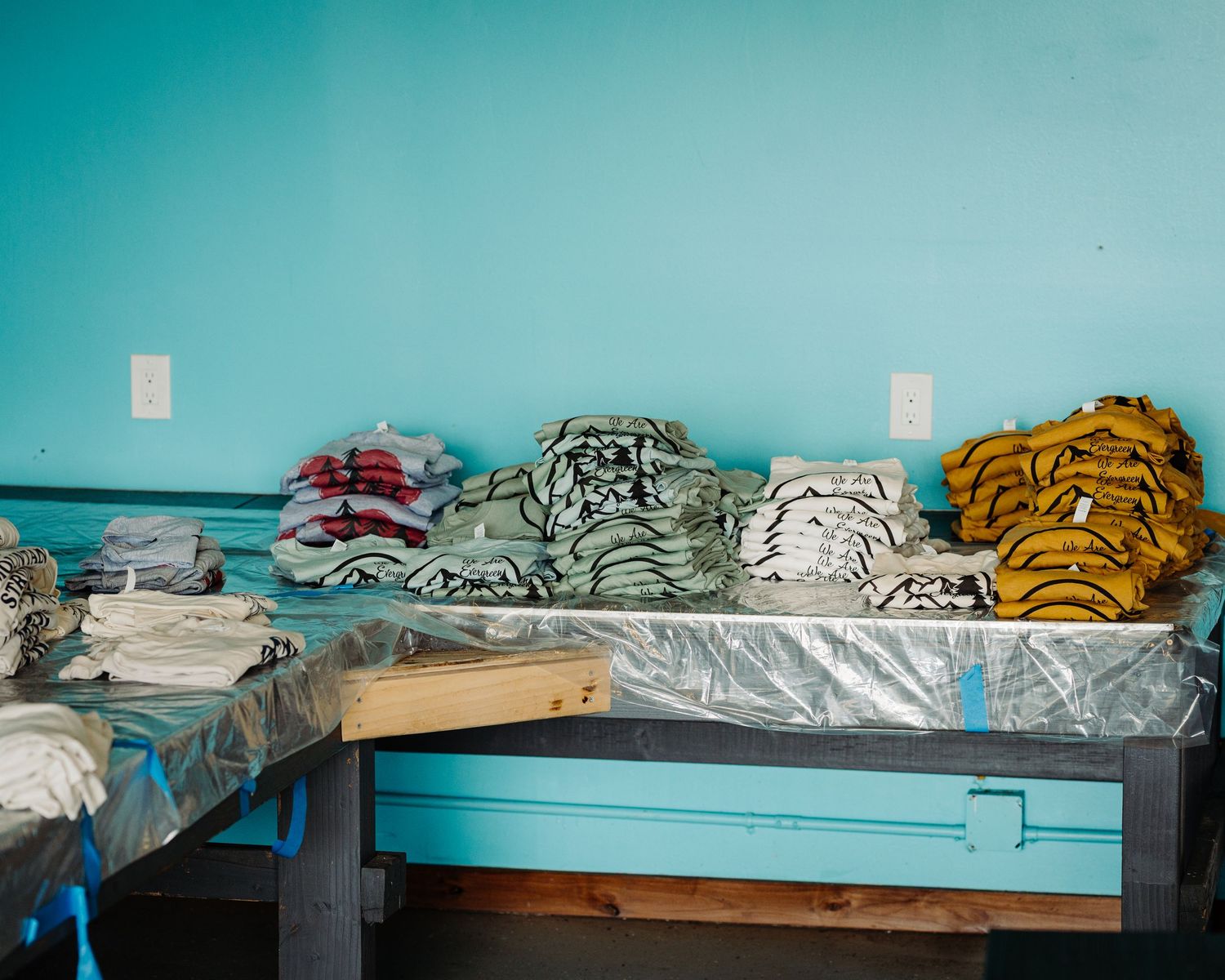 Folded blankets and linens stacked neatly on a wooden bench against a turquoise blue wall.