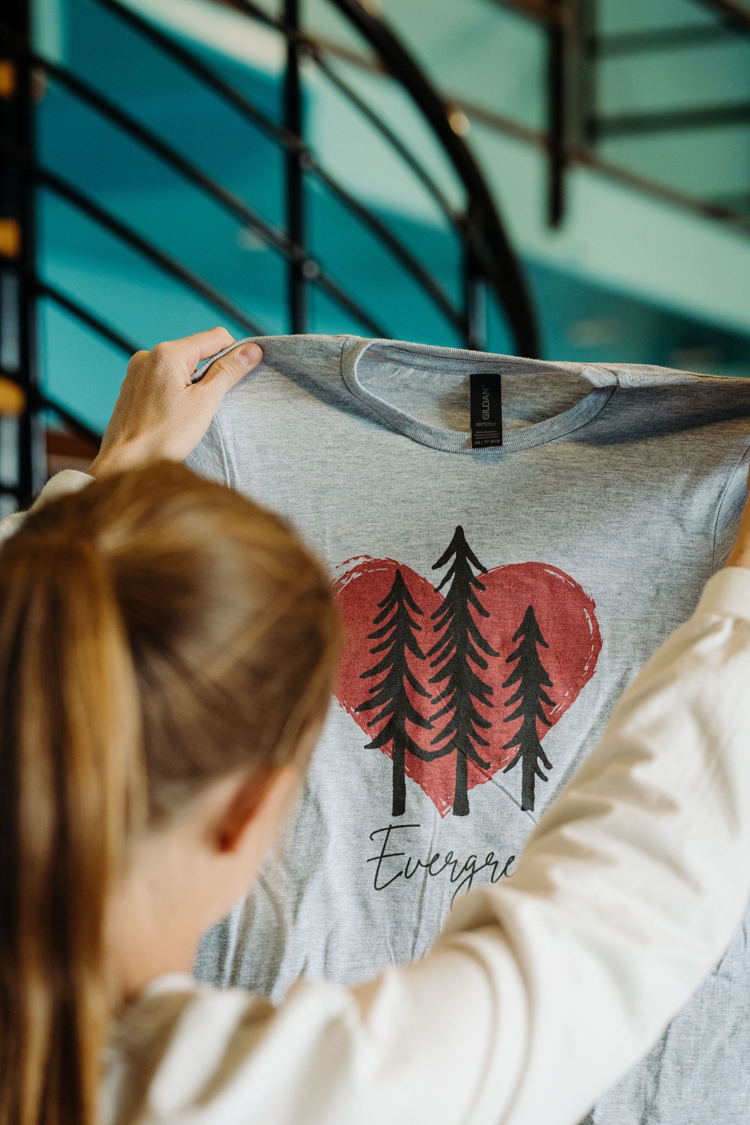 A series of close-up views showing a gray t-shirt with evergreen trees and heart designs printed in coral red.