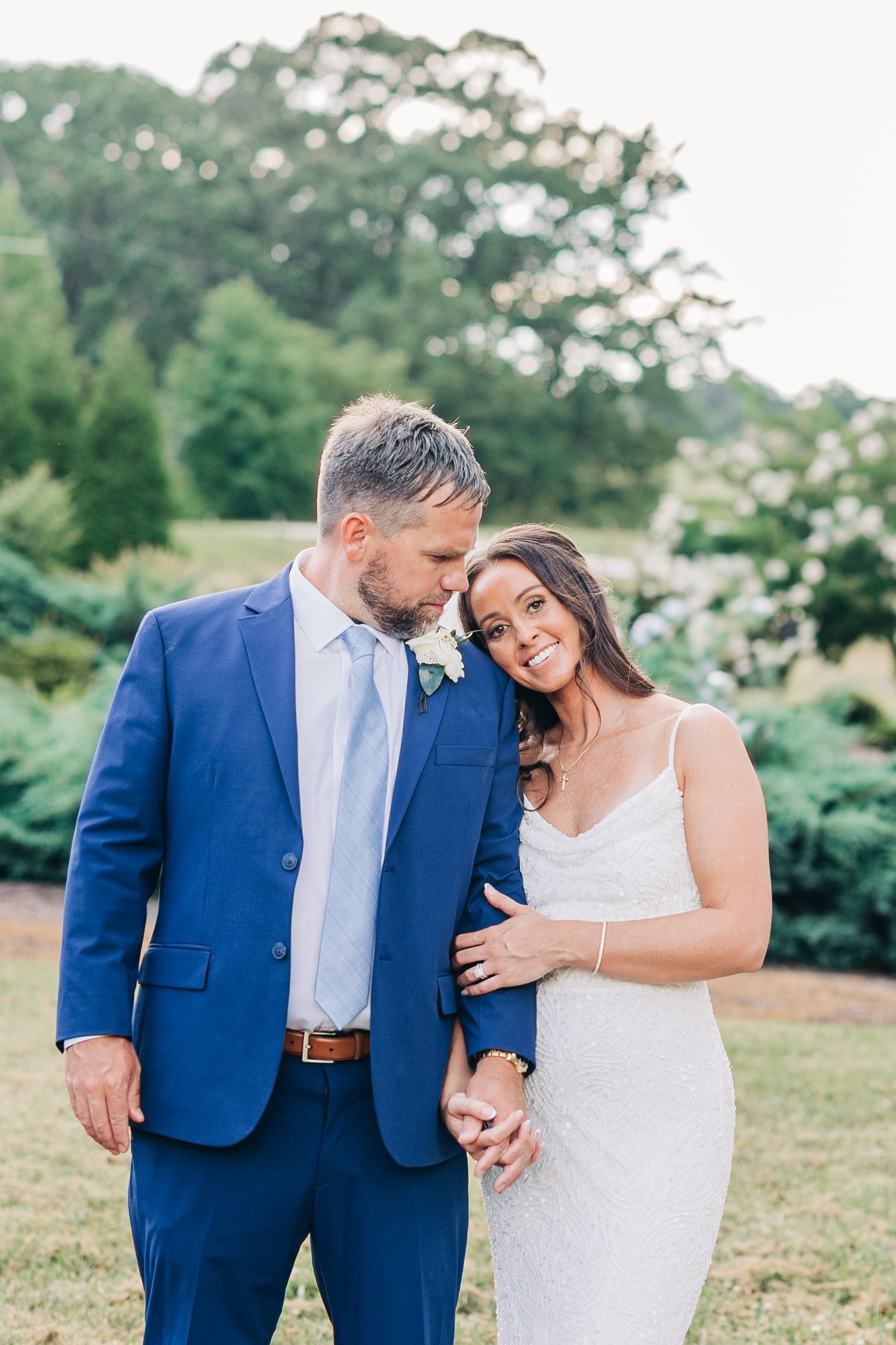 A couple shares romantic moments in an outdoor setting, with the bride in white and groom in navy blue suit.
