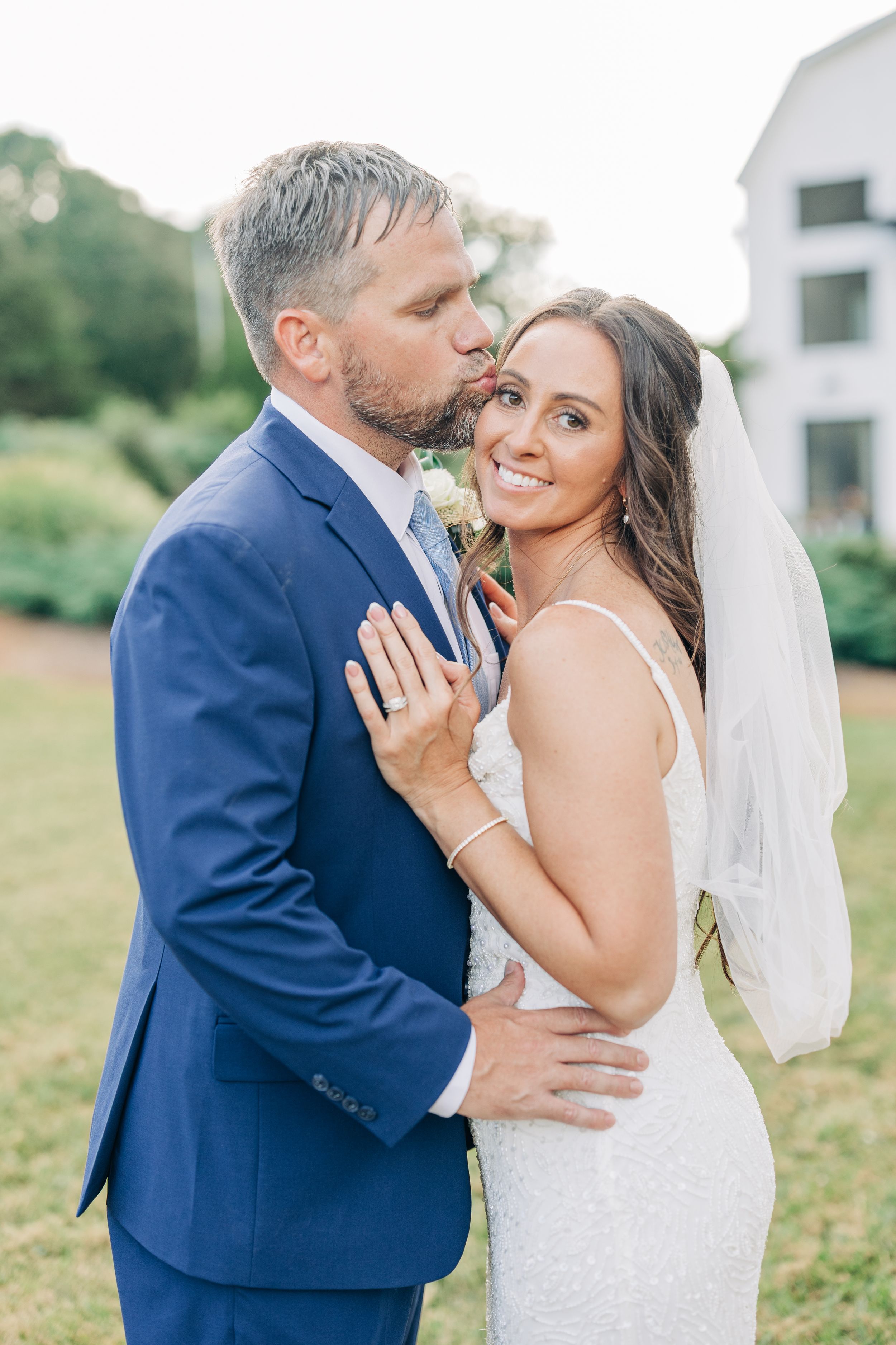 Wedding couple in blue suit and white dress sharing intimate romantic moments outdoors during photoshoot.