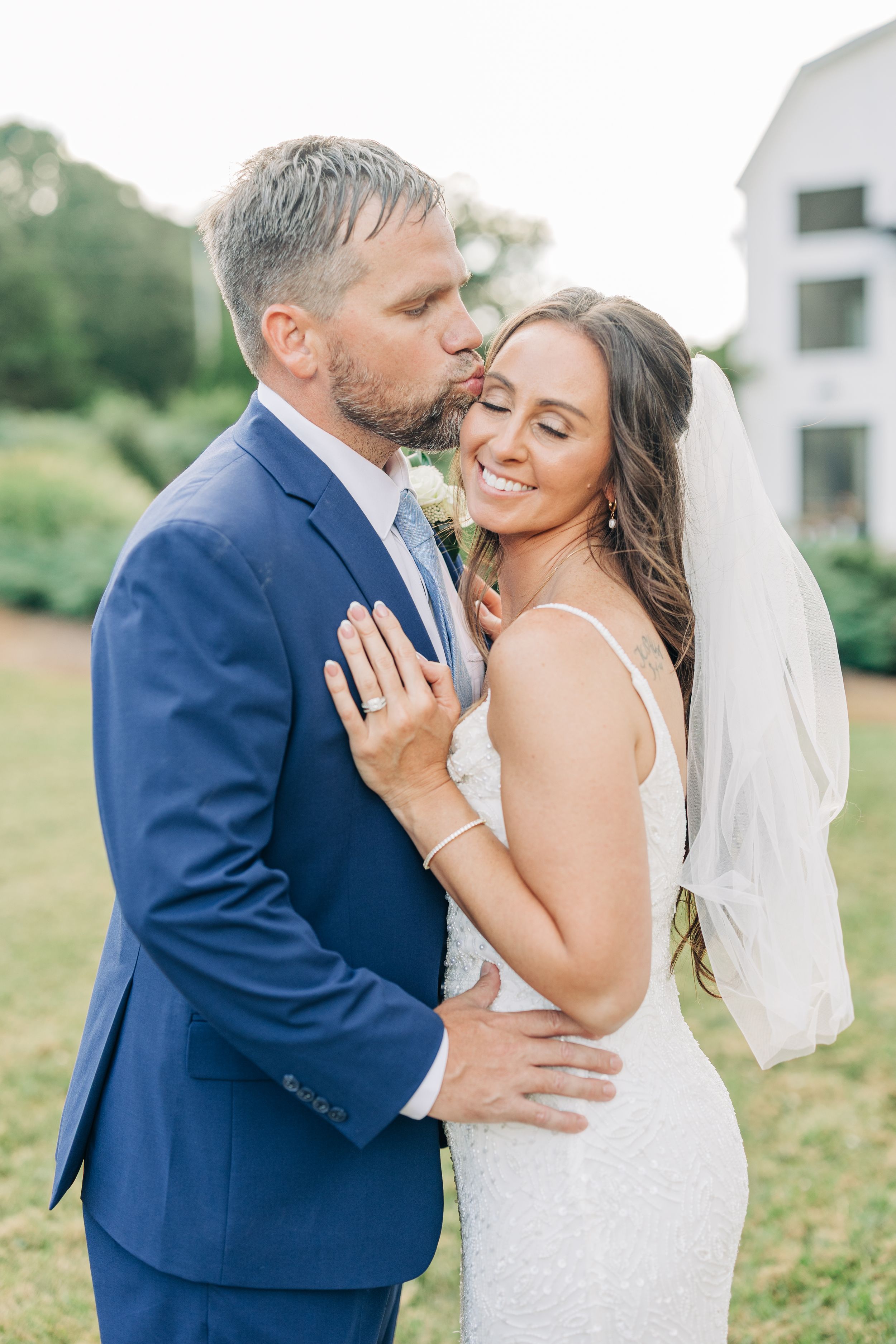 A romantic wedding photoshoot featuring a couple in a navy suit and white dress embracing outdoors.