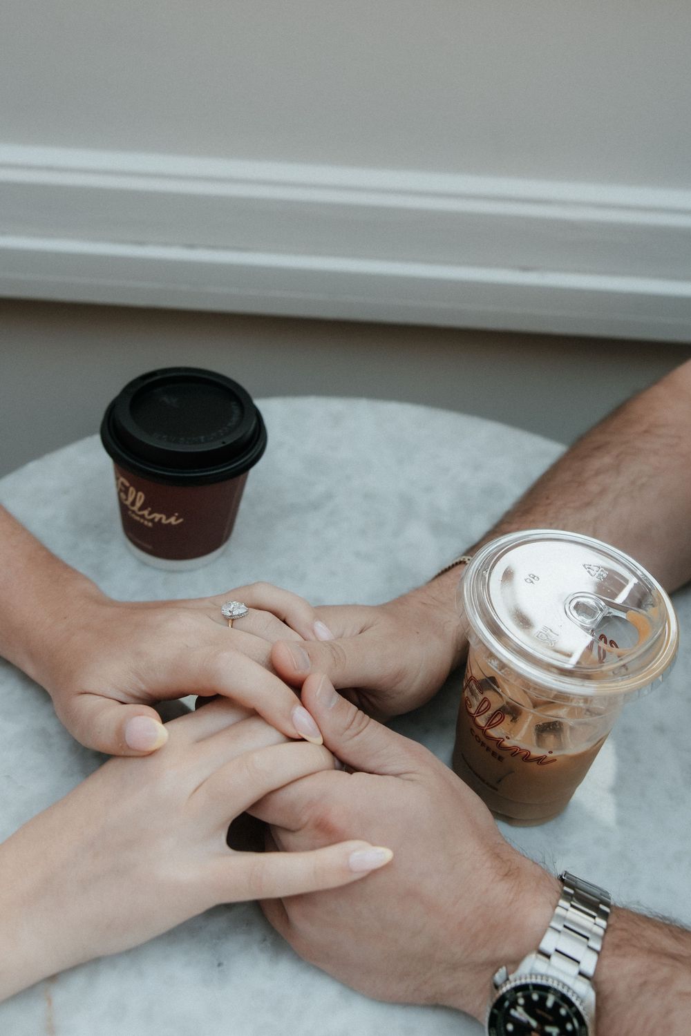 Hands touching intimately on marble table with two coffee drinks in minimalist aesthetic setting.