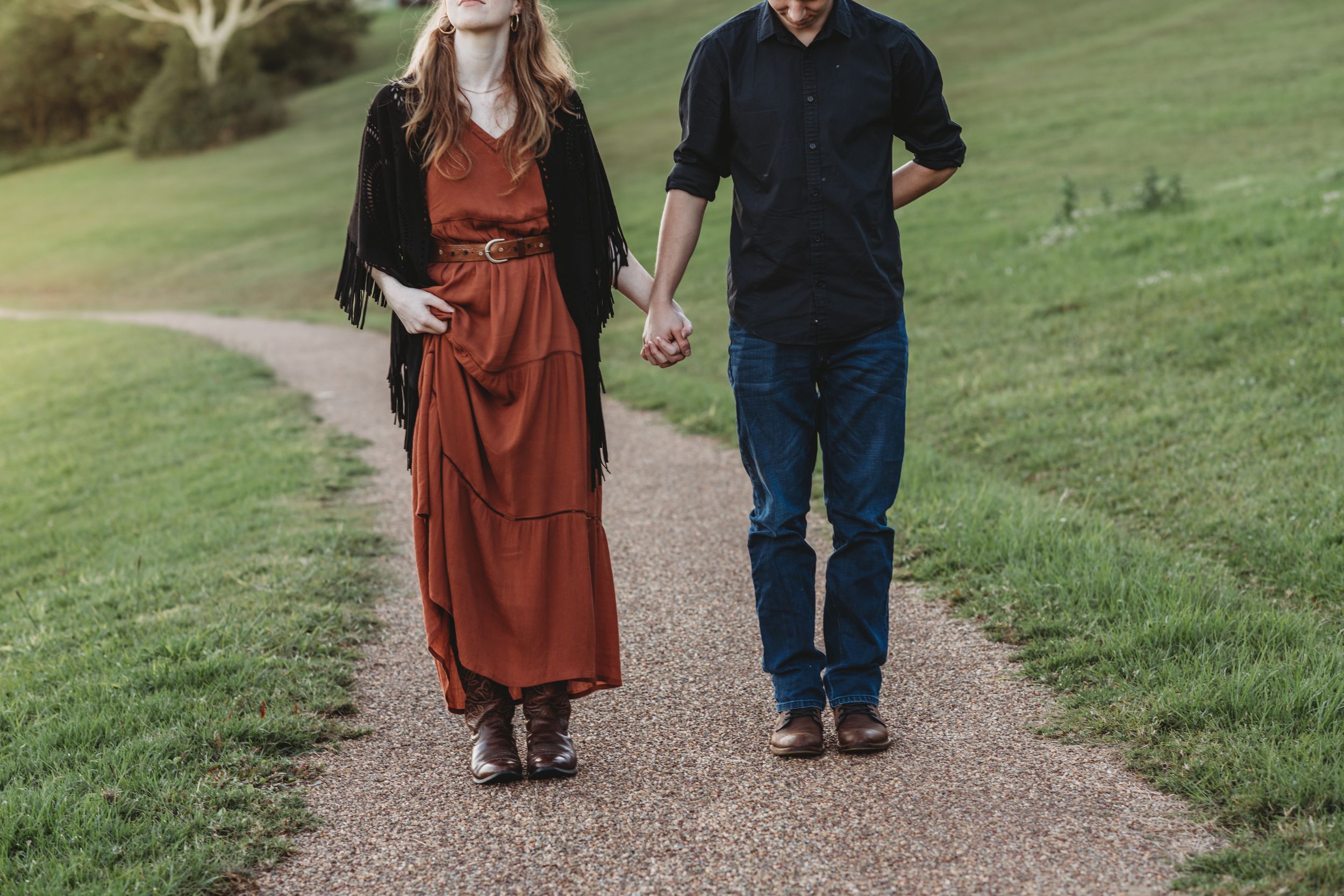 A couple walking hand in hand on a path through green rolling hills.