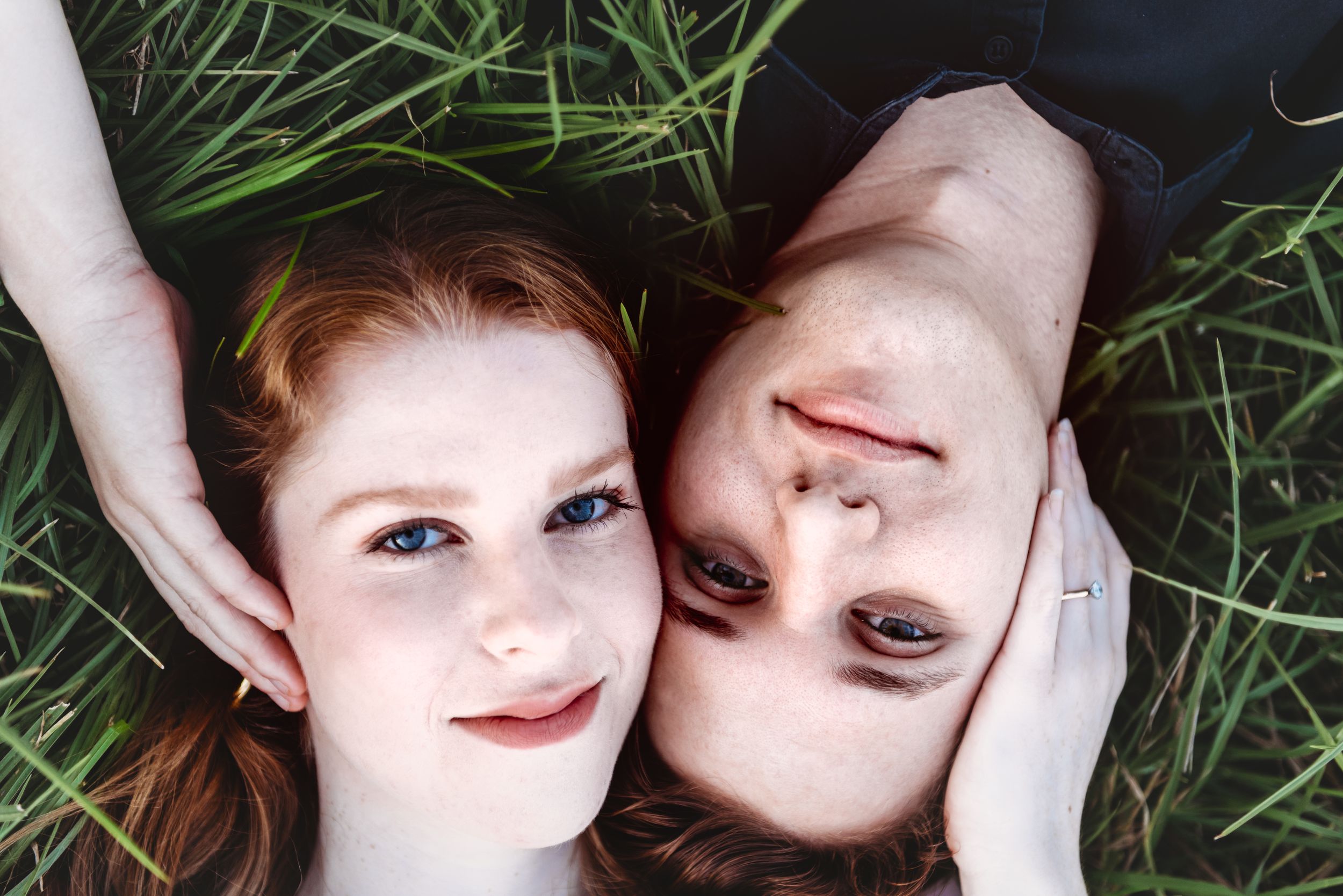 A couple lying in green grass photographed from above in an artistic portrait.