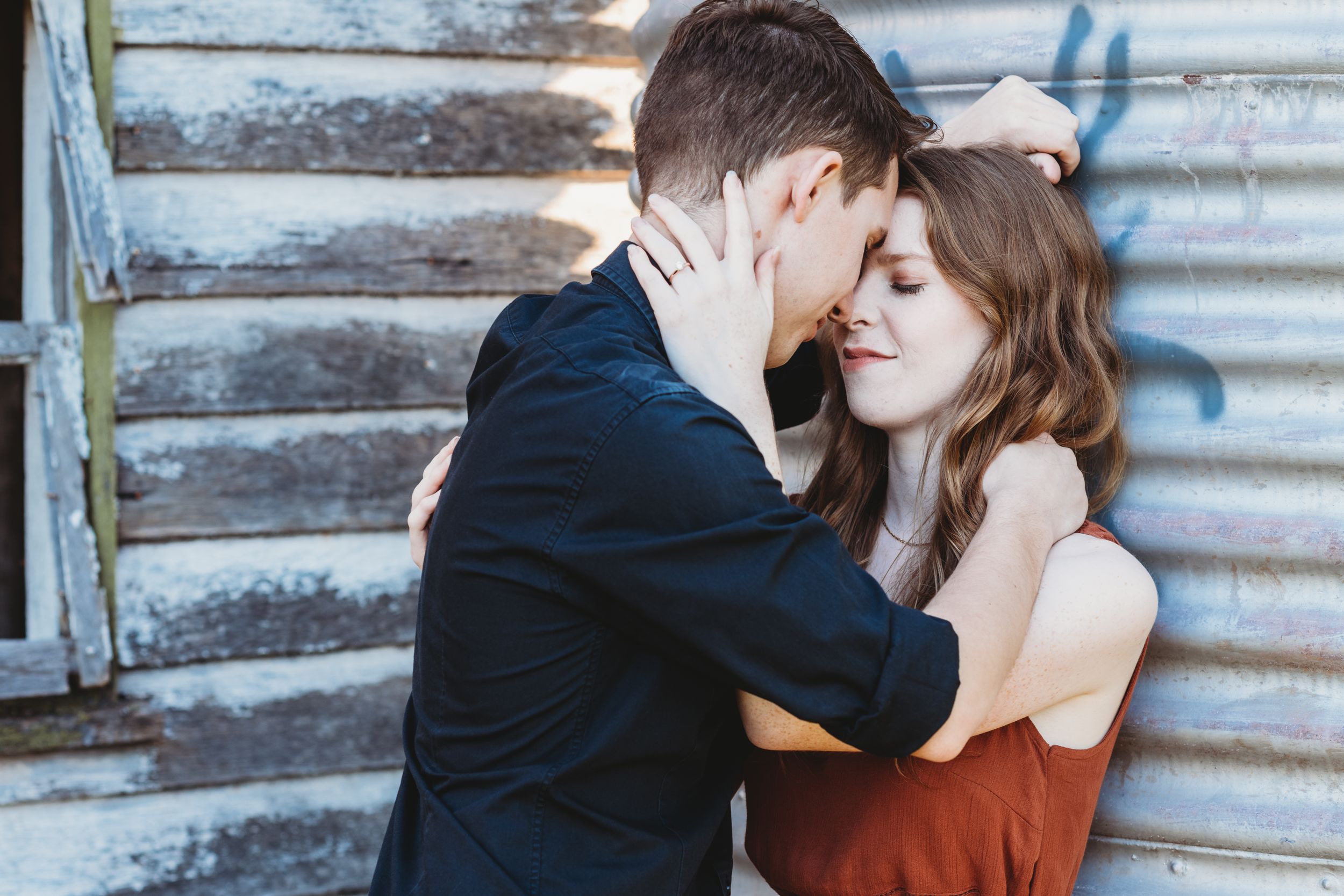A romantic couple sharing an intimate moment against a rustic wall.