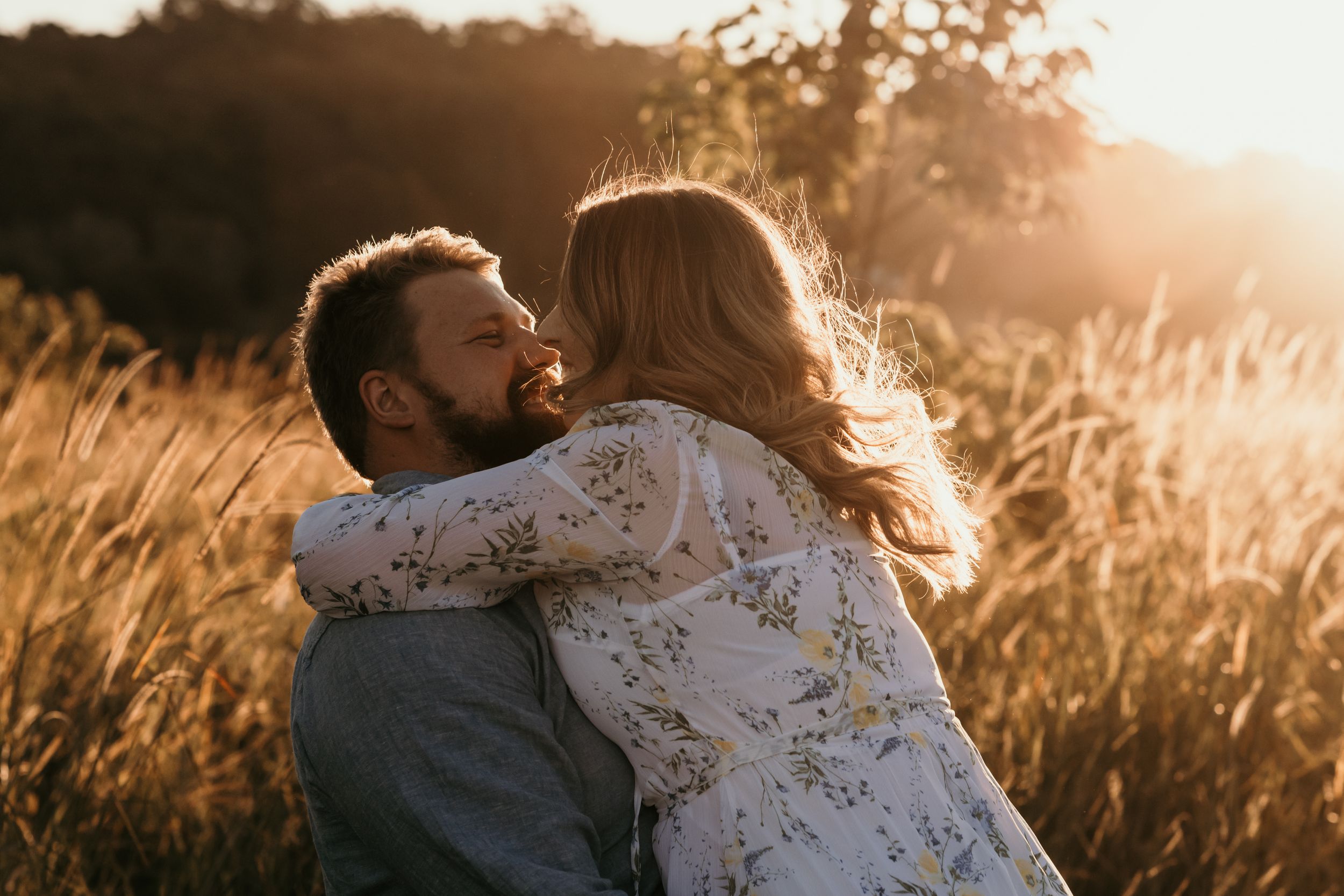 Couple embracing in golden sunlit field during sunset photoshoot.