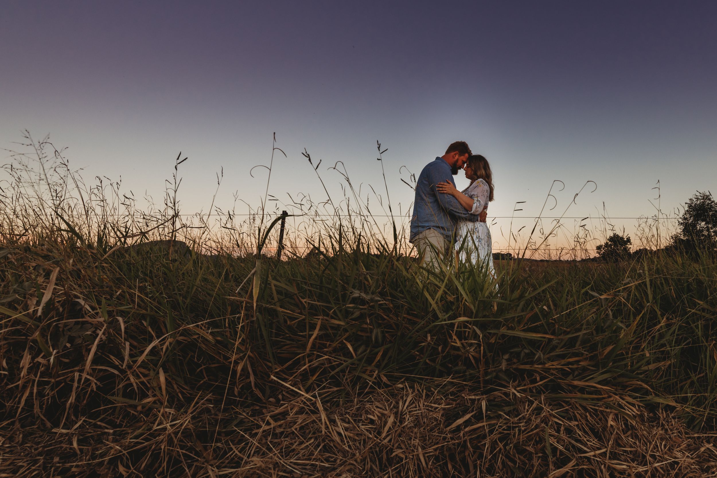 Silhouetted couple embracing in a field of tall grass during sunset.