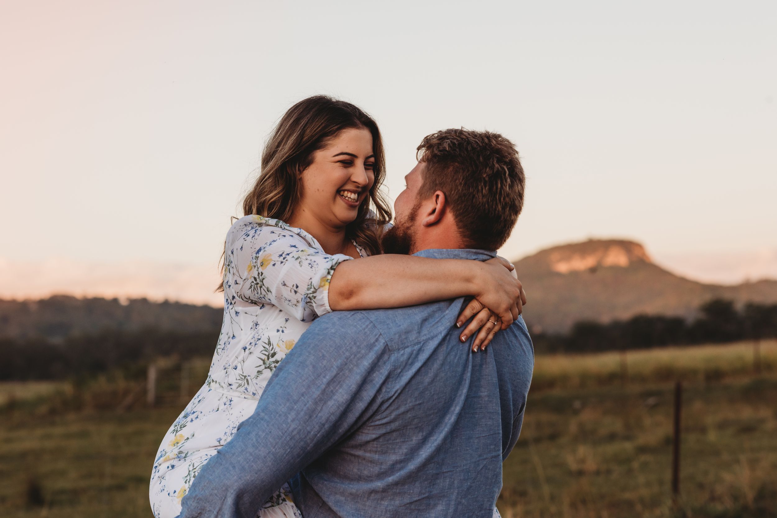 Couple laughing and embracing outdoors during sunset engagement photo session.