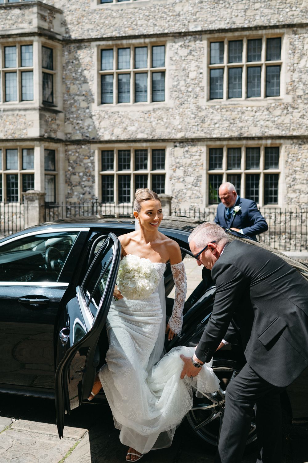 A sequence of photos showing a bride in white dress getting assistance entering a black car outside a stone building.