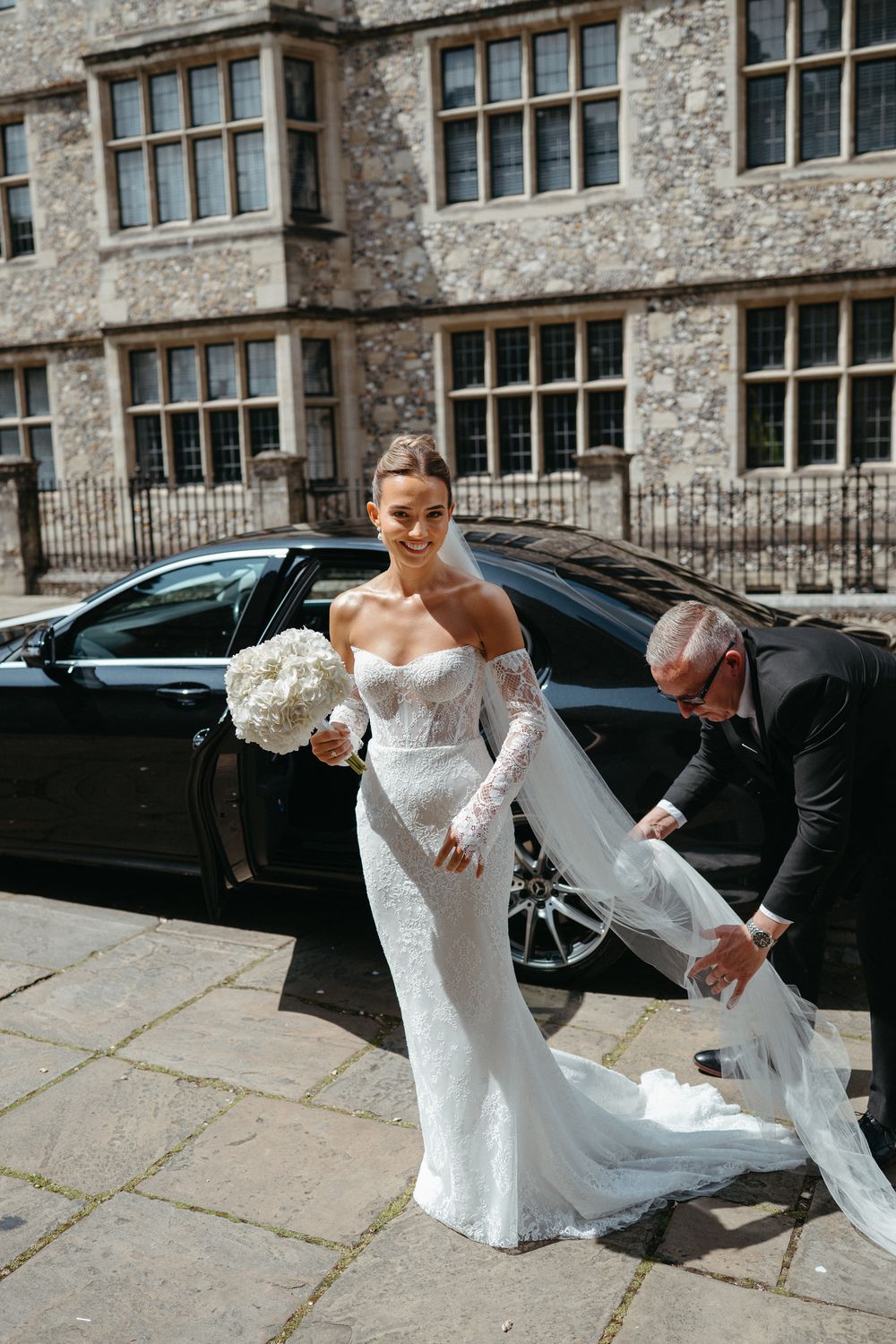 Sequential shots capture someone helping a bride in lace dress getting into a luxury vehicle at a historic venue.
