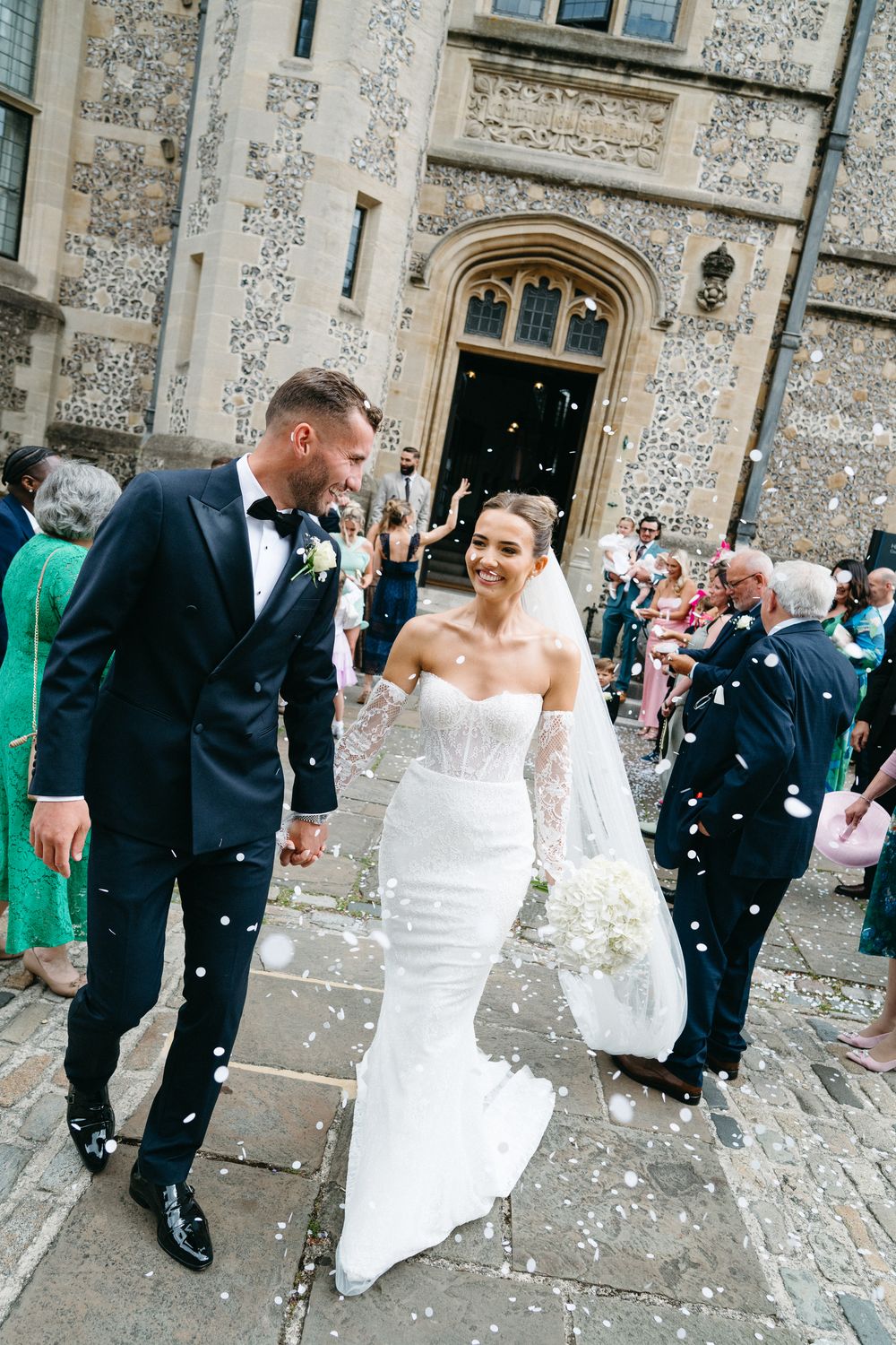 Wedding guests shower newlyweds with confetti as they exit a historic stone church building.