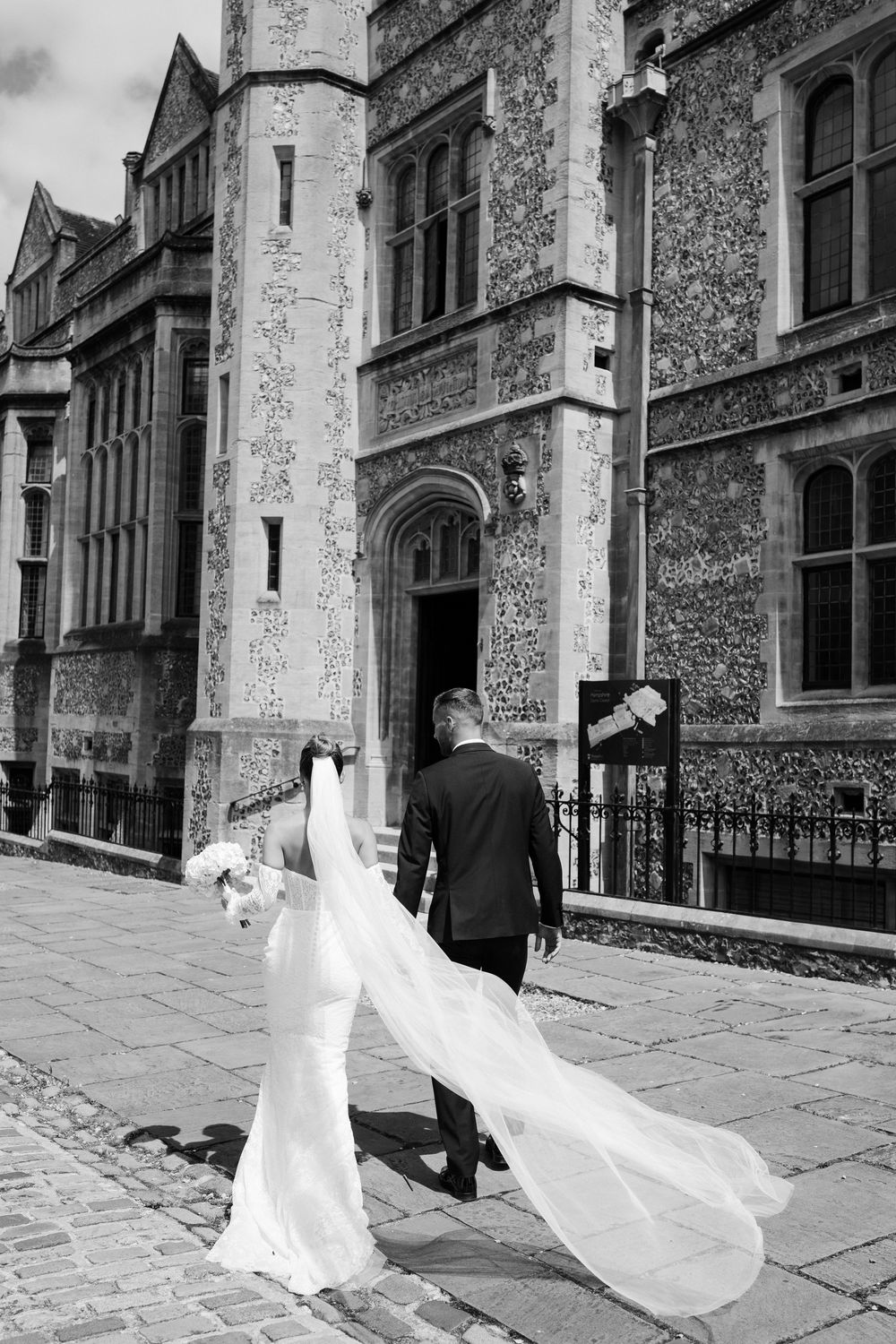Three black and white photographs show a bride's flowing wedding dress veil floating in the wind along cobblestone street.