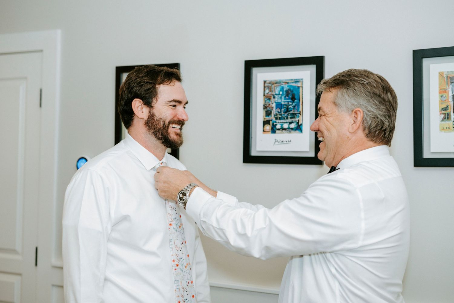 Two men in white dress shirts share a joyful moment together on a bright day.